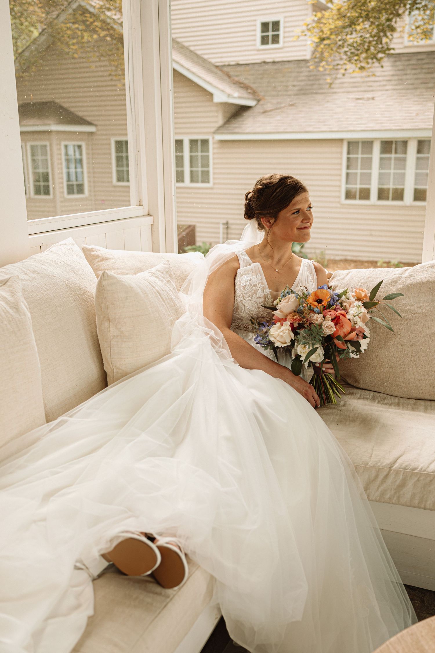 Beautiful white wedding gown with layers of tulle fabric flowing elegantly across a plush cream colored sofa.