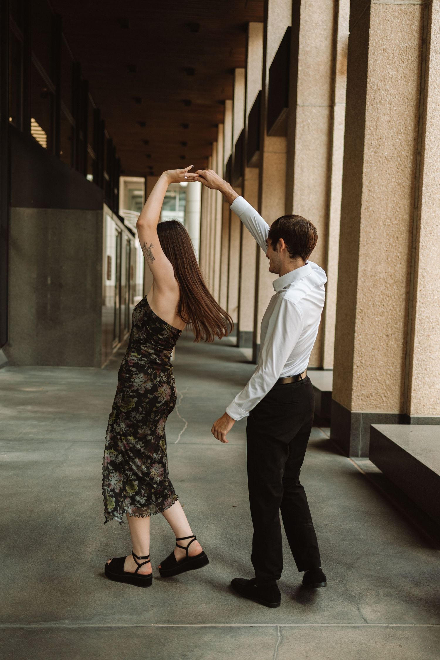 A couple dances together in a covered outdoor hallway with stone columns, creating a romantic atmosphere.