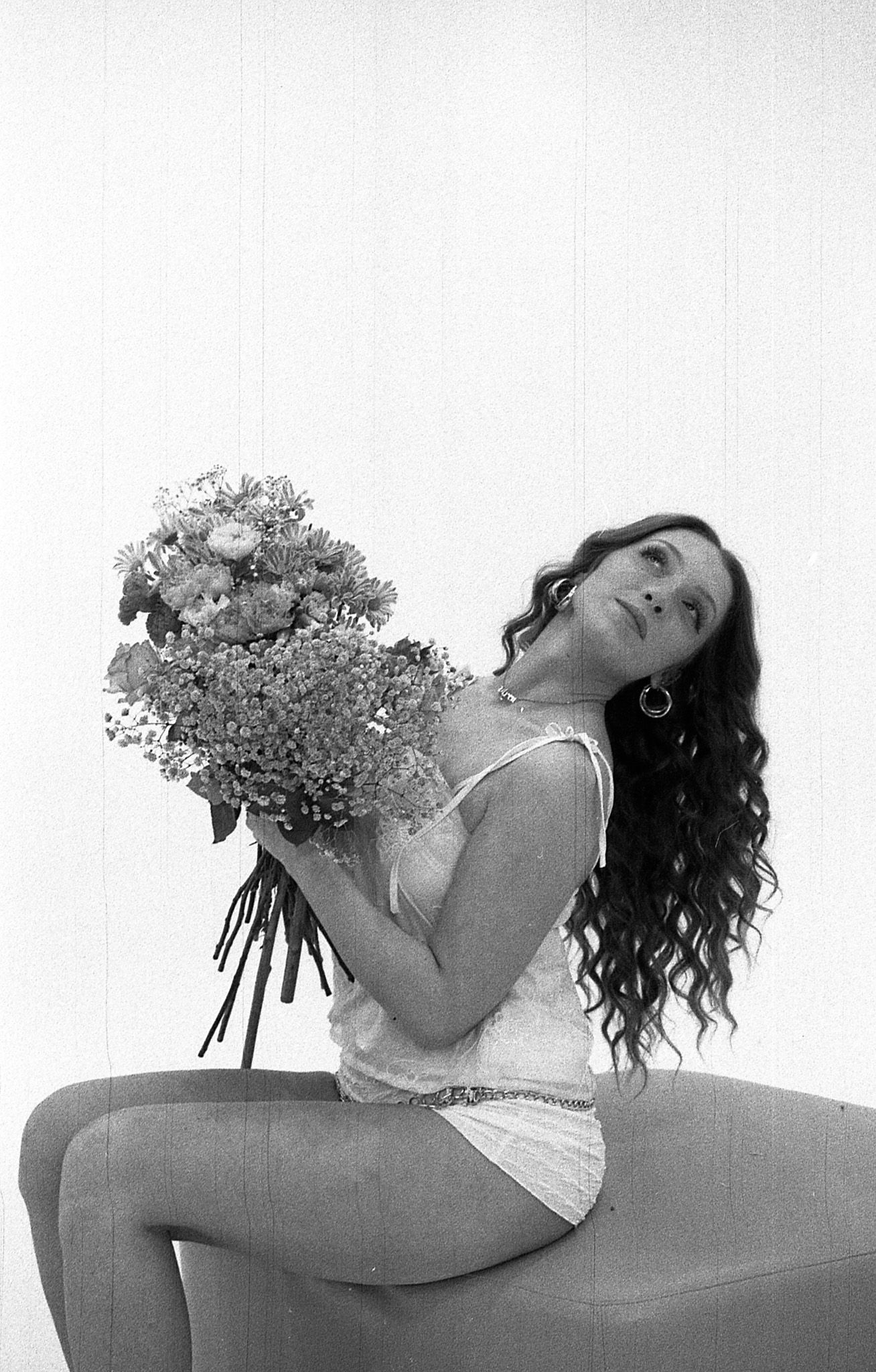 A black and white artistic photograph of someone posing with a large bouquet of delicate flowers.