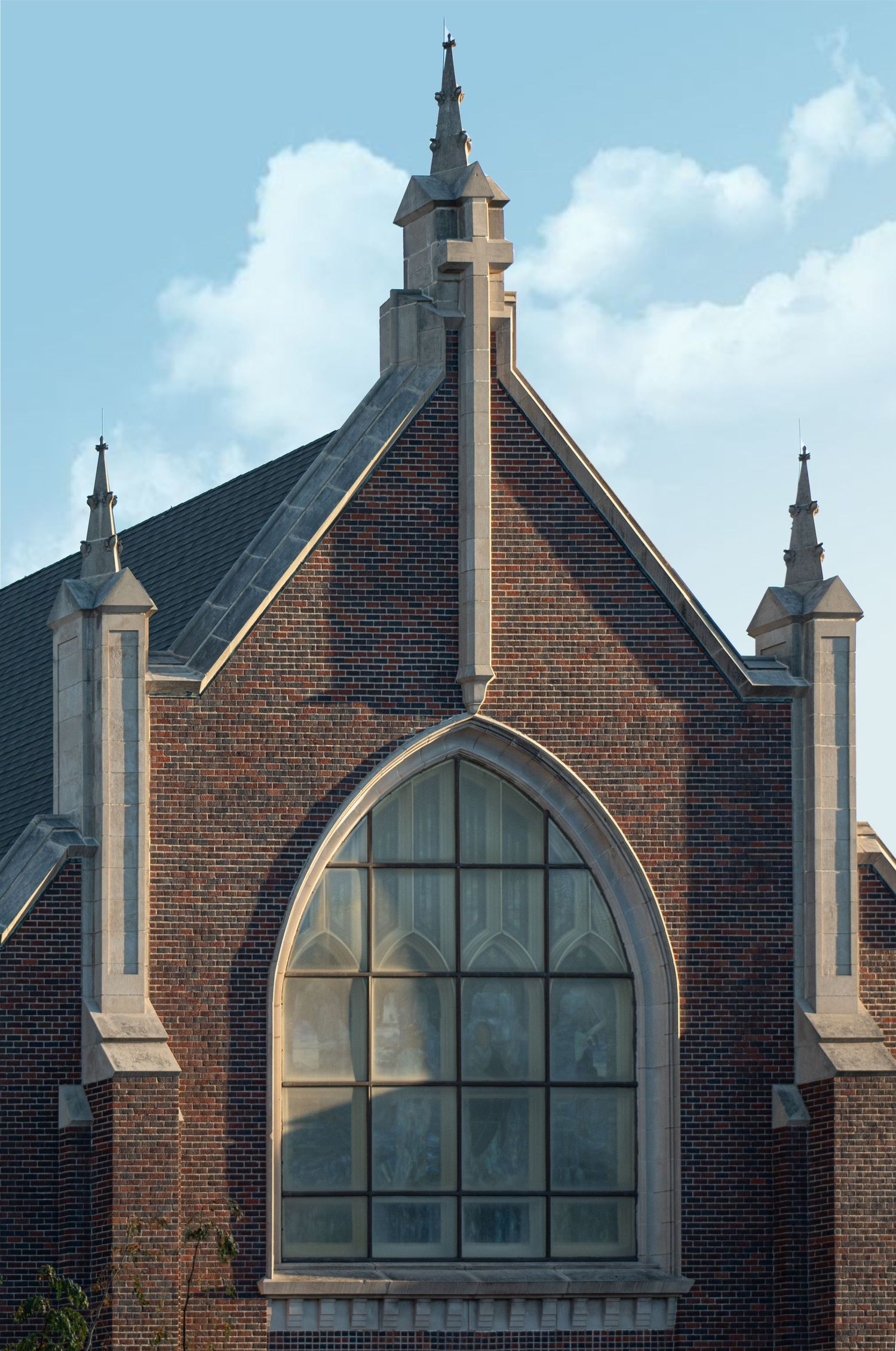 Gothic arch window and spires adorn the brick facade of a church steeple against a bright blue sky.