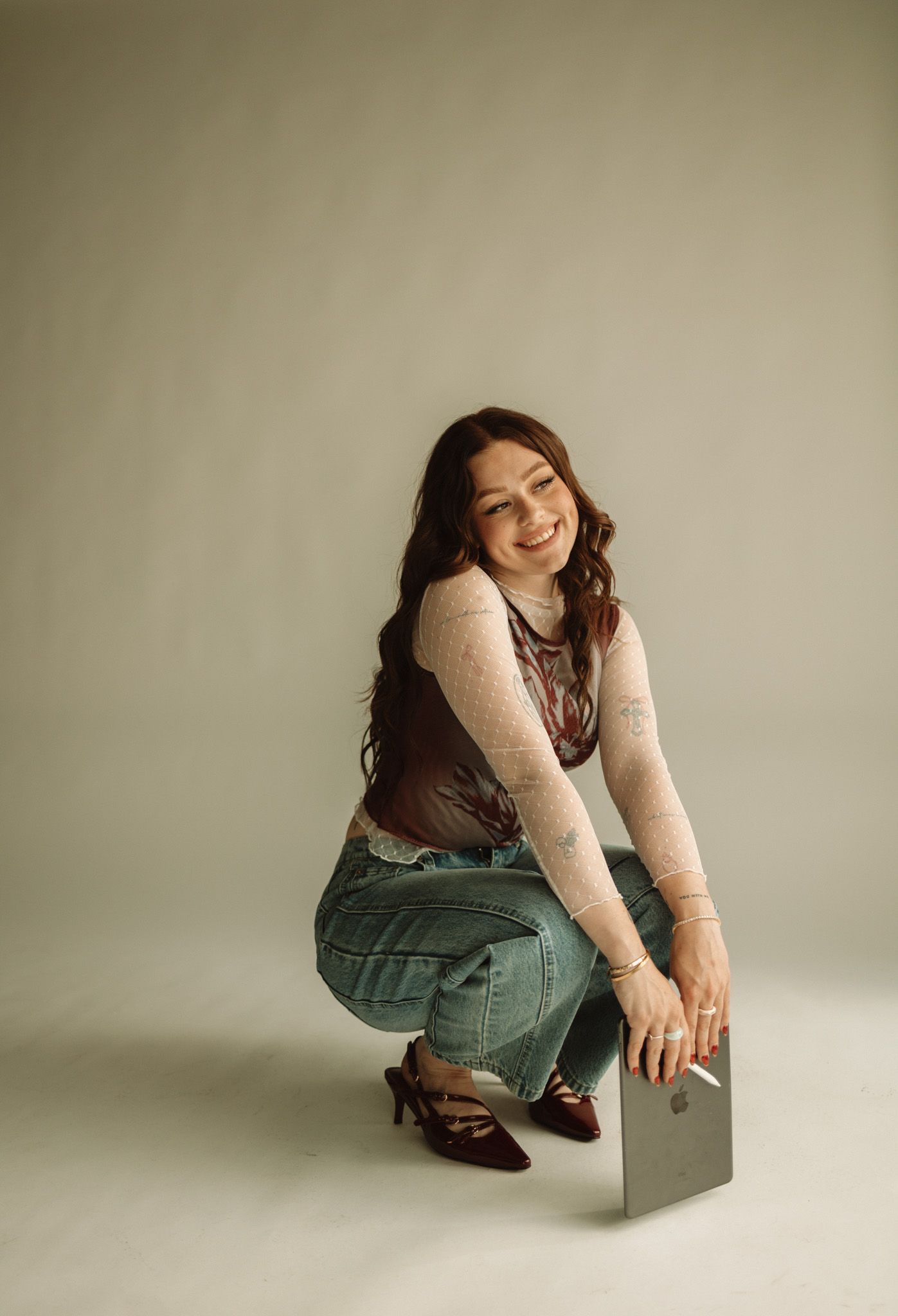 A person in a cream sweater and jeans crouches next to a small box against a neutral studio backdrop.