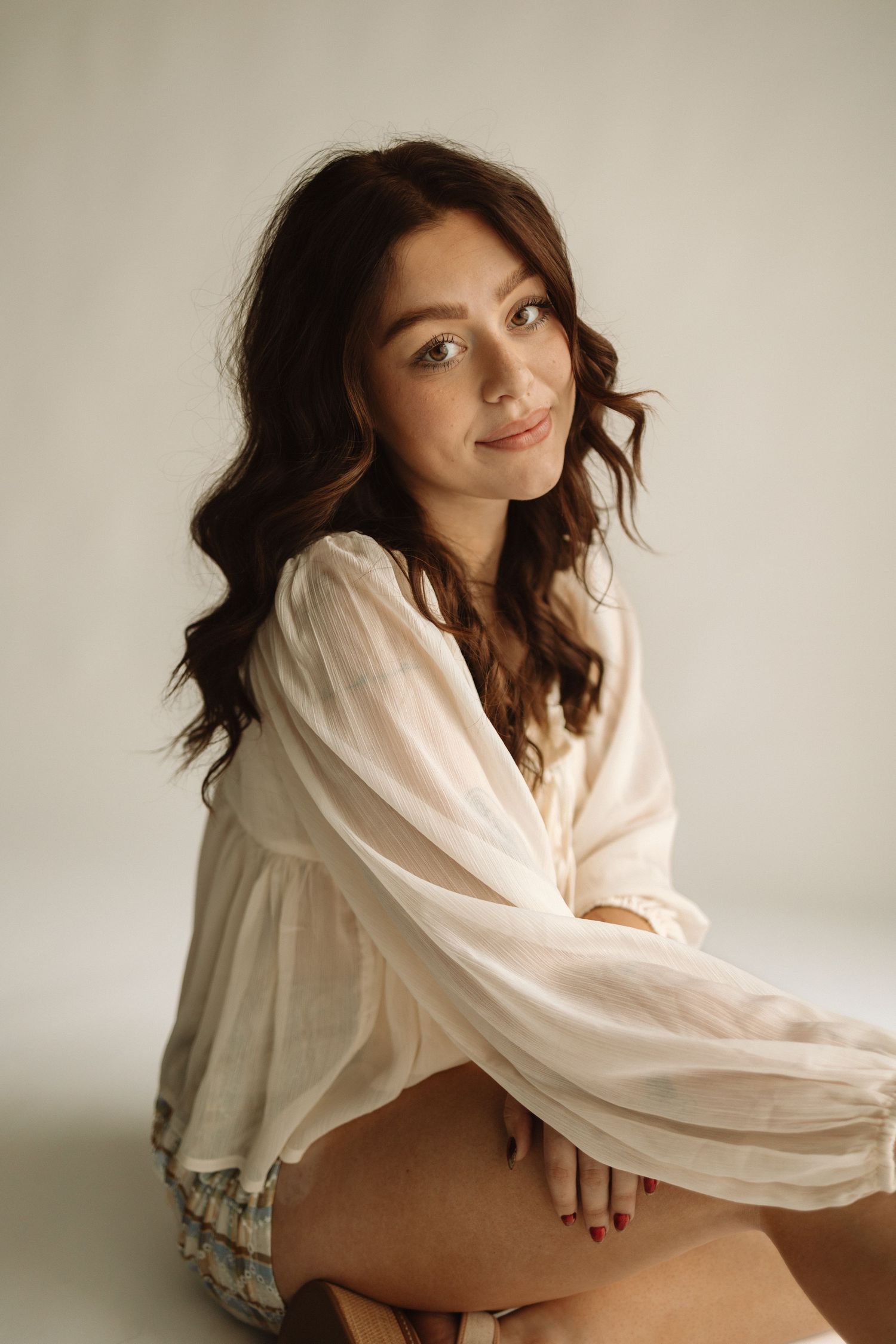 Portrait in soft lighting features flowing white blouse with billowing sleeves against neutral background.