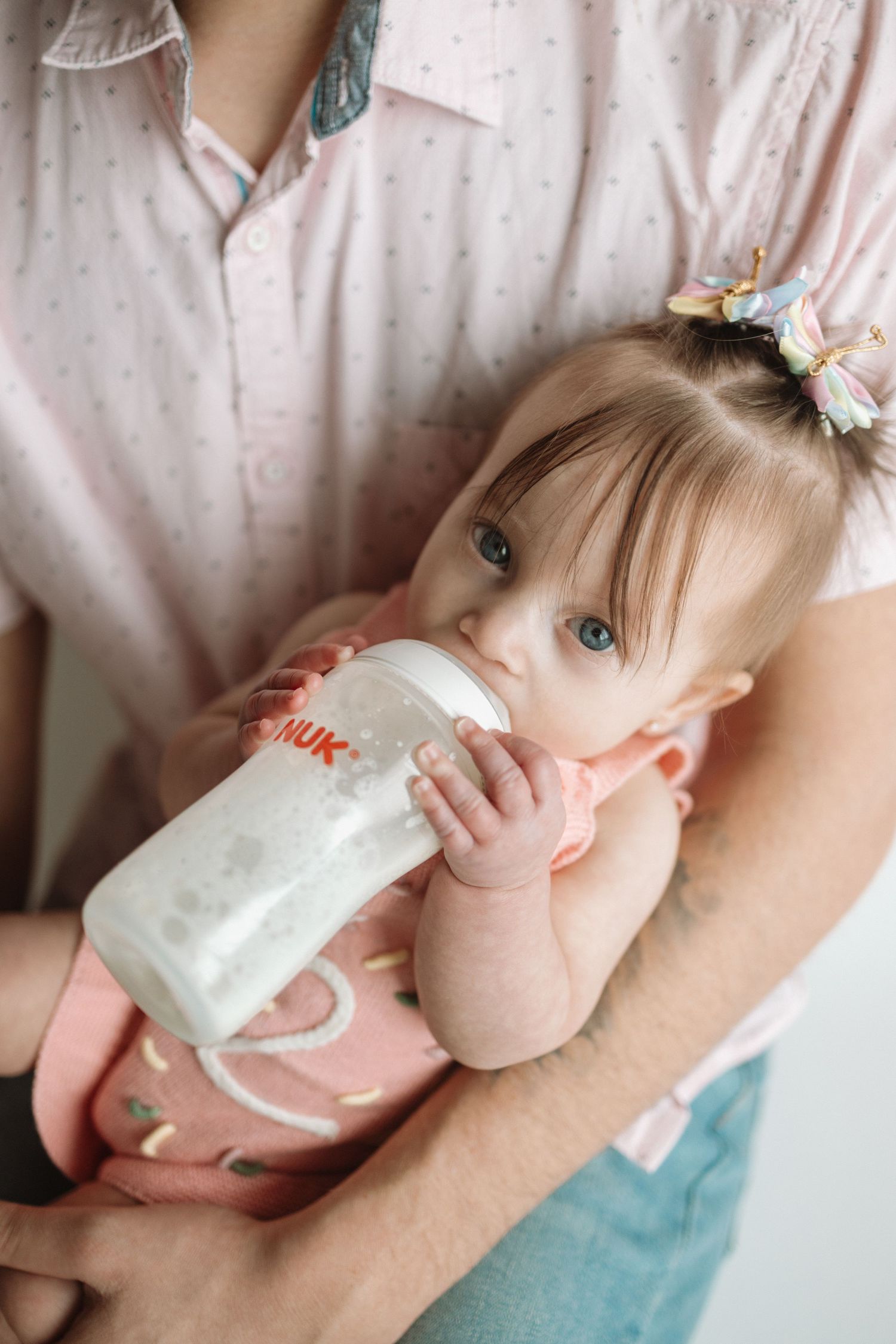 Baby drinks milk from bottle while resting on blue cushion in four sequential photos.
