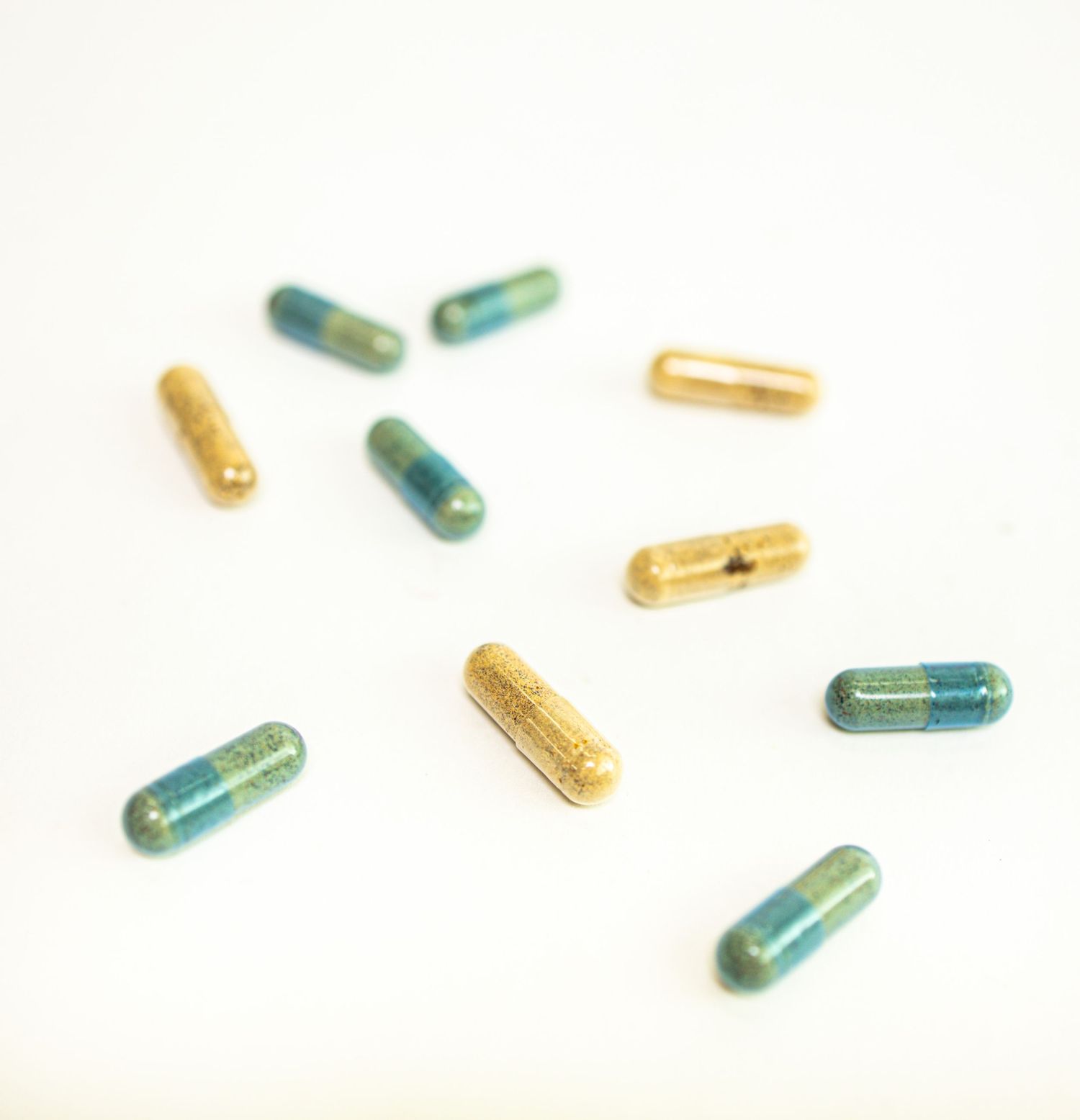 Scattered blue and gold medication capsules on a white surface creating a minimalist pharmaceutical composition.