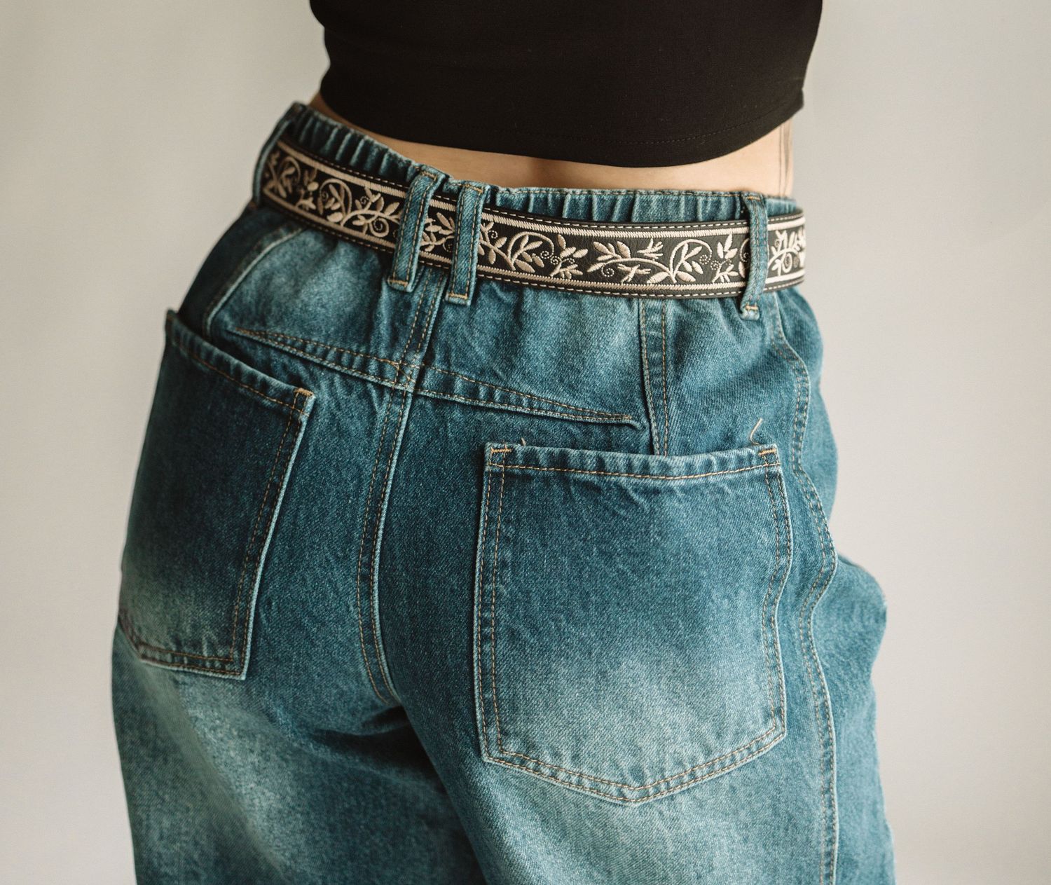 High-waisted vintage style blue denim jeans with decorative belt and back pockets shown from behind.