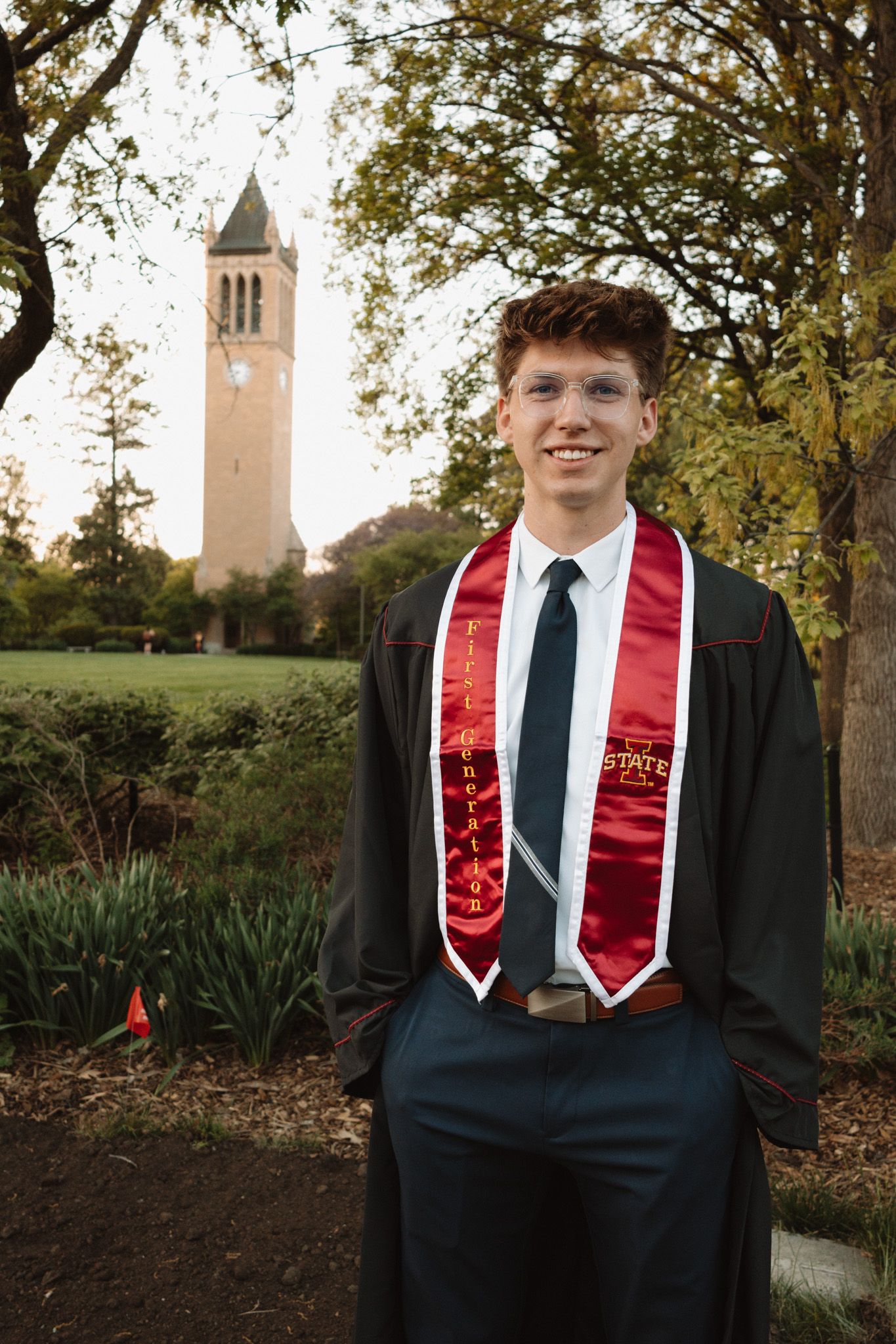 Graduation photo at Iowa State University with the iconic Campanile bell tower visible in the background on a fall day.