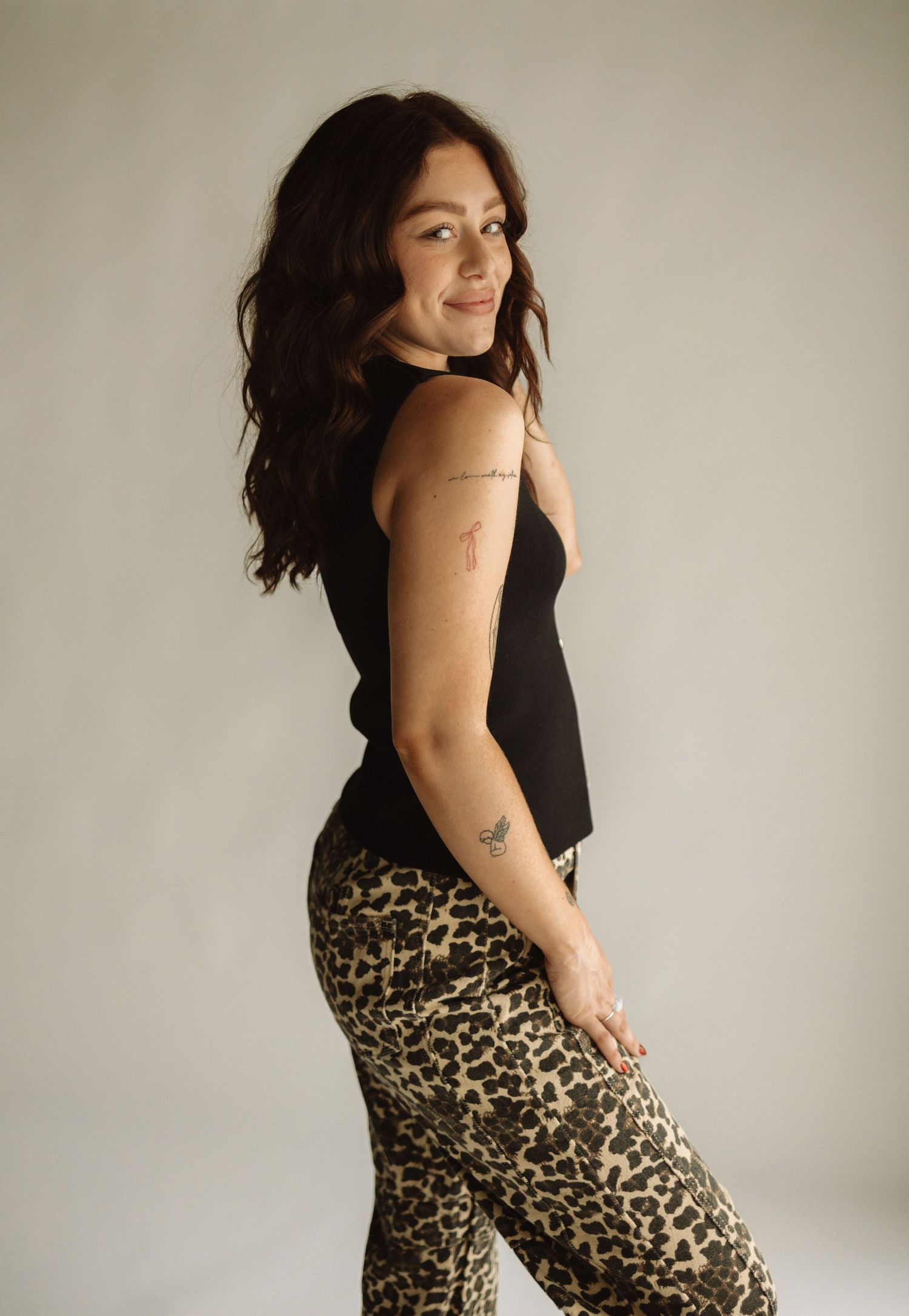 A woman poses in black tank top and leopard print pants against a neutral wall showing different angles and expressions.