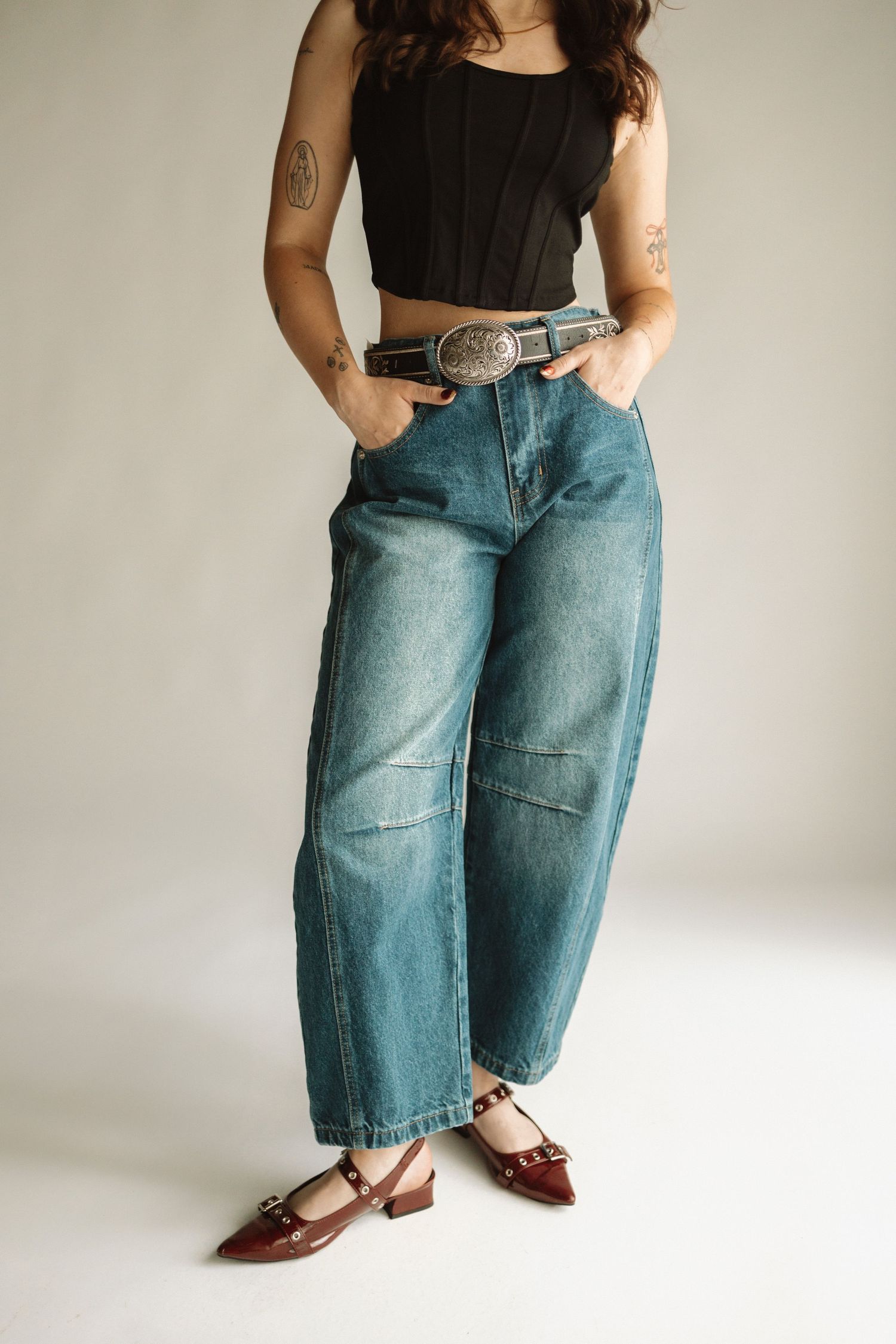 Model wearing wide-leg vintage jeans with decorative belt buckle and casual footwear against white studio background.