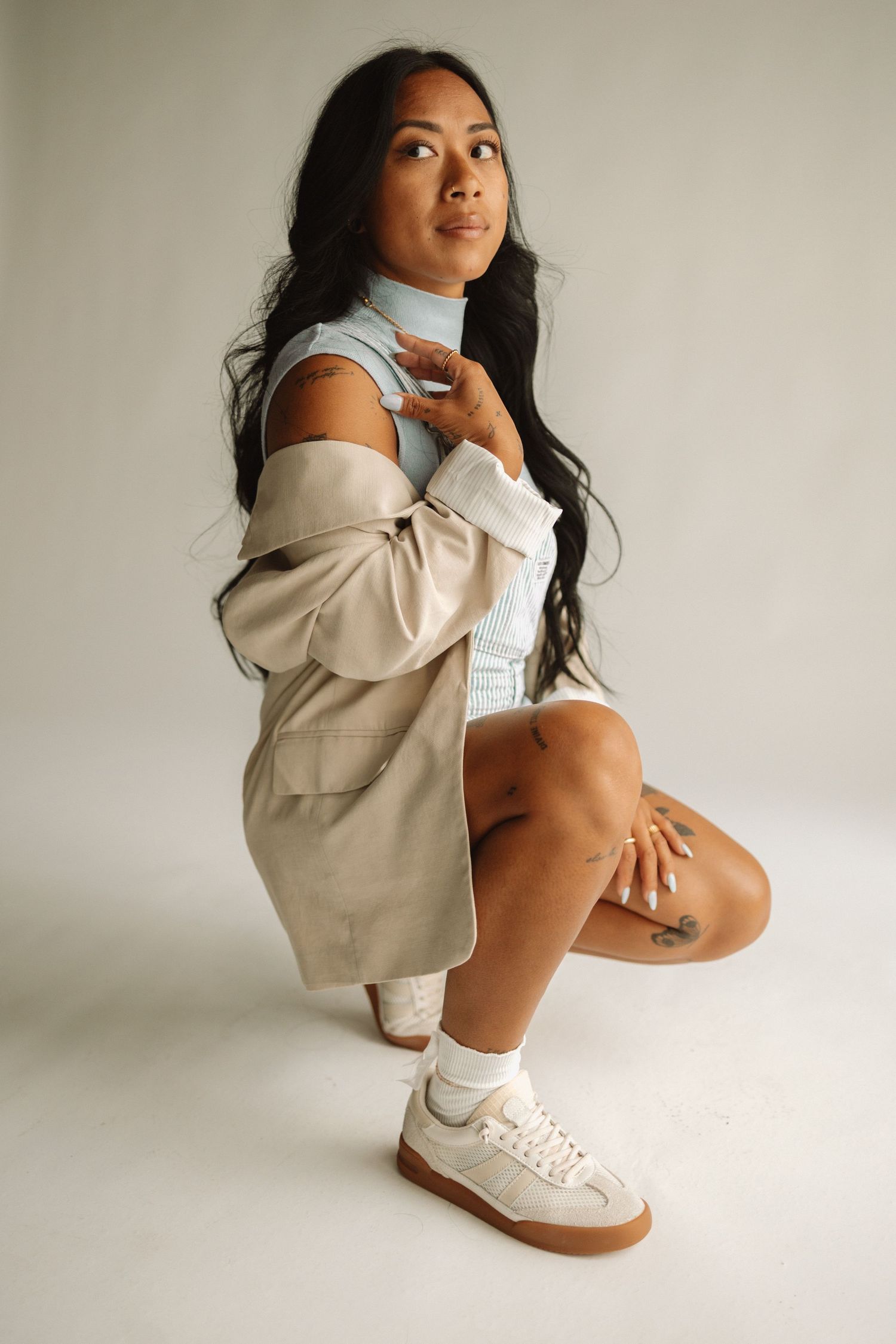 A minimalist fashion photo series showing poses in white sneakers, beige hoodie and white socks against neutral backdrop.