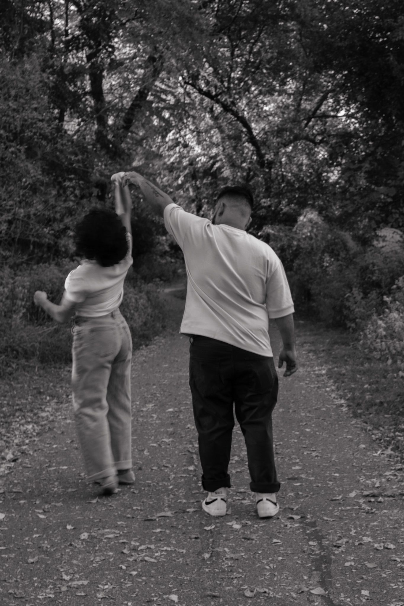 Couple dancing together on a tree-lined path in black and white.