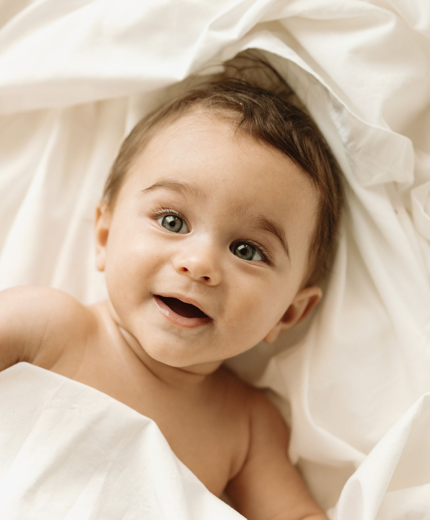 Baby wrapped in soft white blankets looks peaceful while lying down on white bedding.