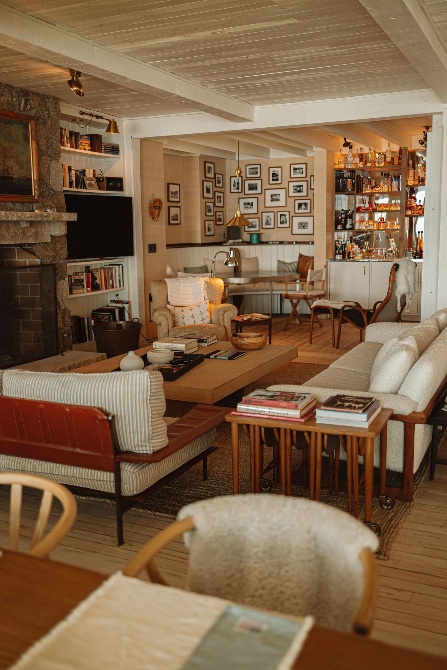 Cozy rustic lounge area with wooden ceiling beams, bookshelves, and comfortable seating arrangements in warm tones.
