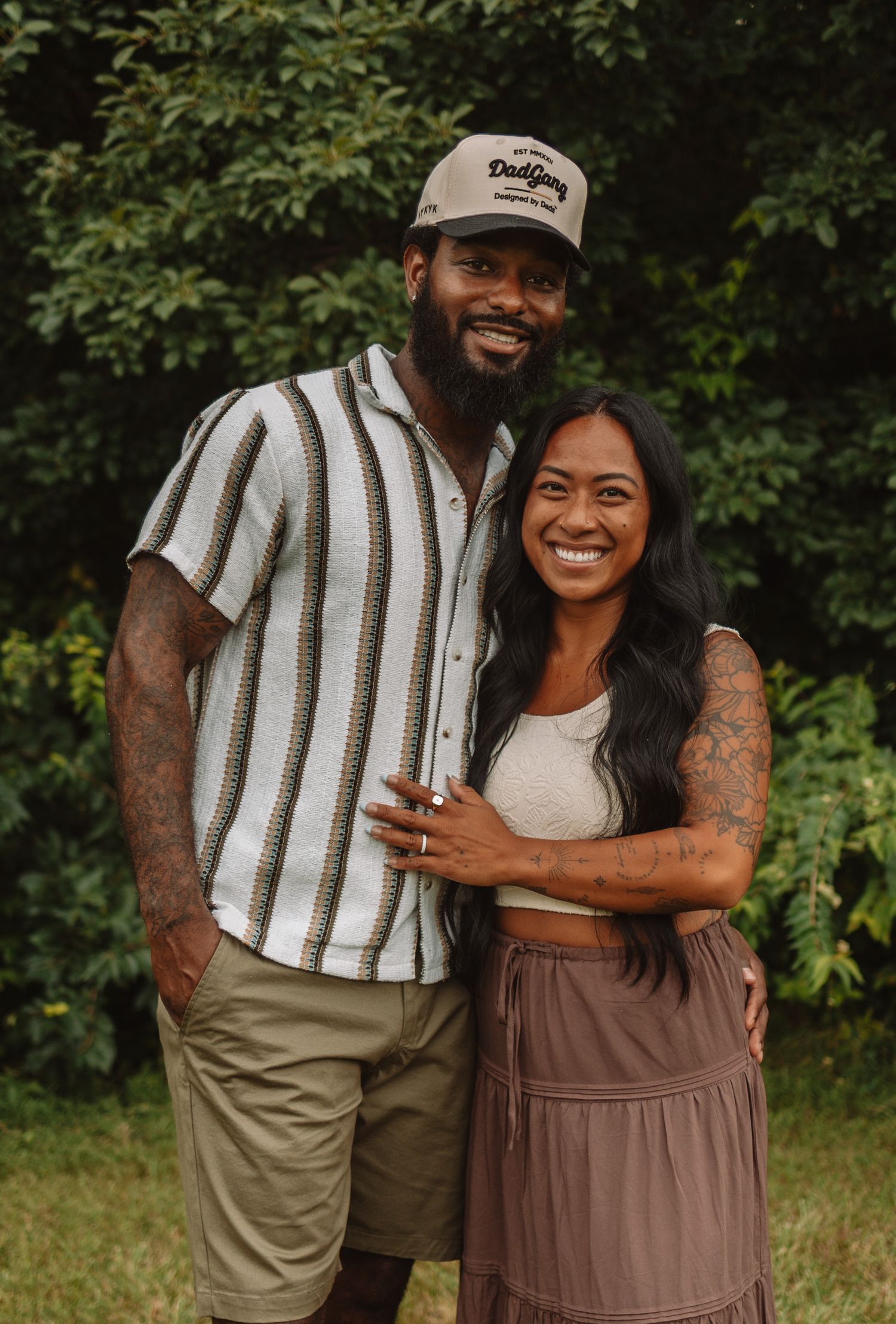 A couple laughs together outdoors while embracing against a green natural background.