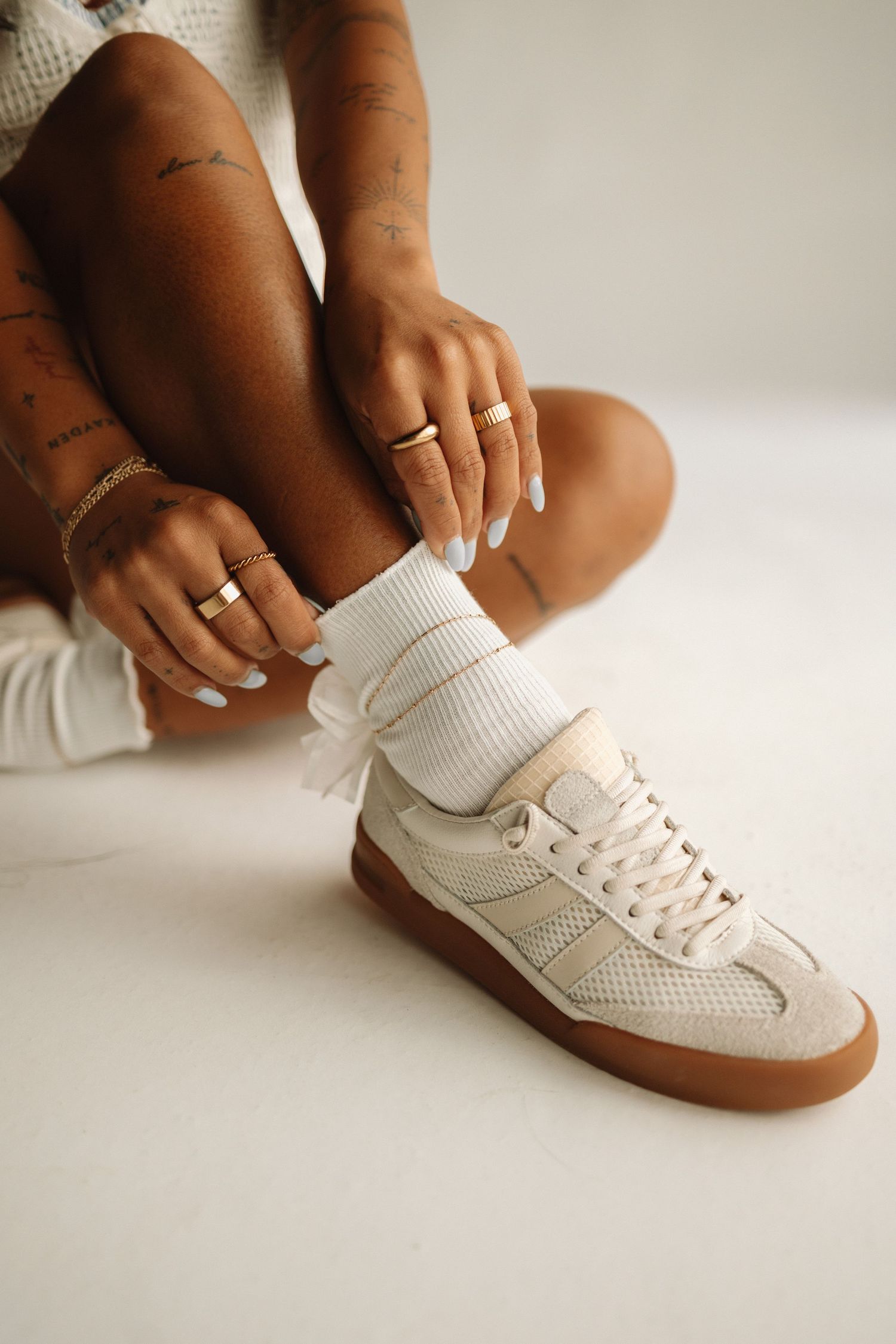 A series of photos showing white leather and gum sole sneakers being put on feet styled with rings and jewelry.