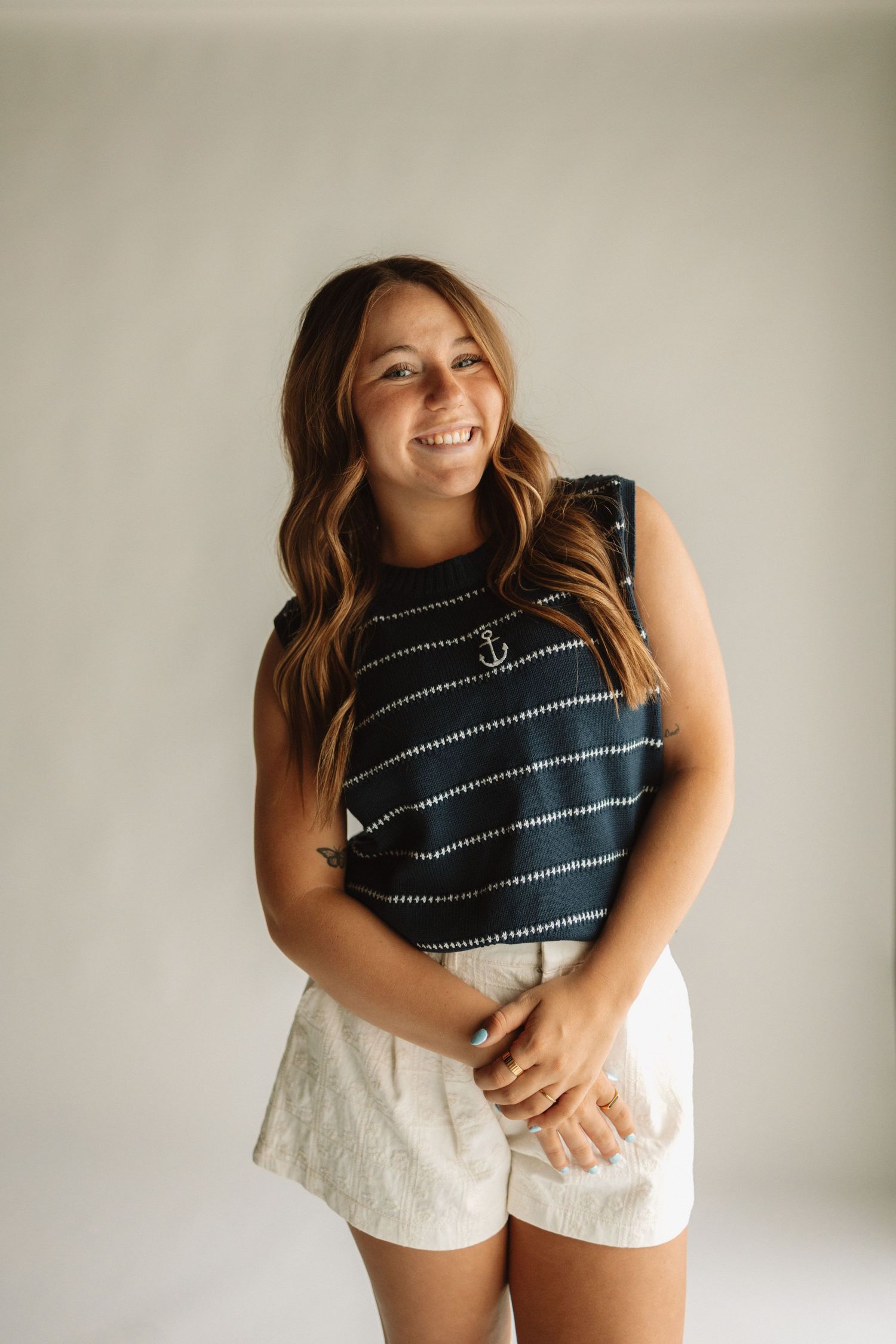 Lifestyle portrait of someone in a navy striped sleeveless top and white shorts against a neutral wall.