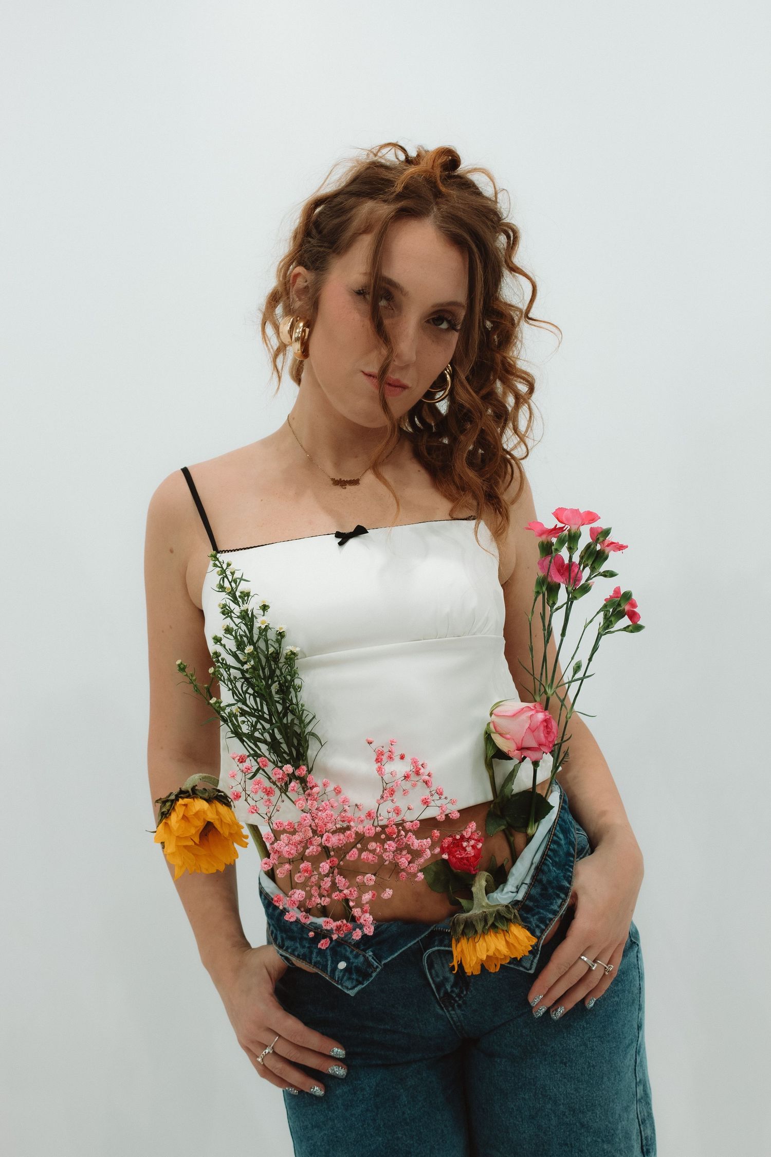 A romantic spring-style portrait with curly hair, white top and blue jeans filled with fresh colorful flowers.