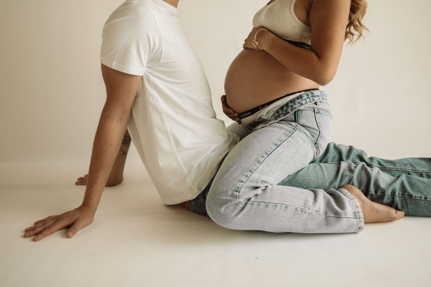A series of minimalist photos showing people seated on the floor against a white wall wearing casual denim and white clothing.