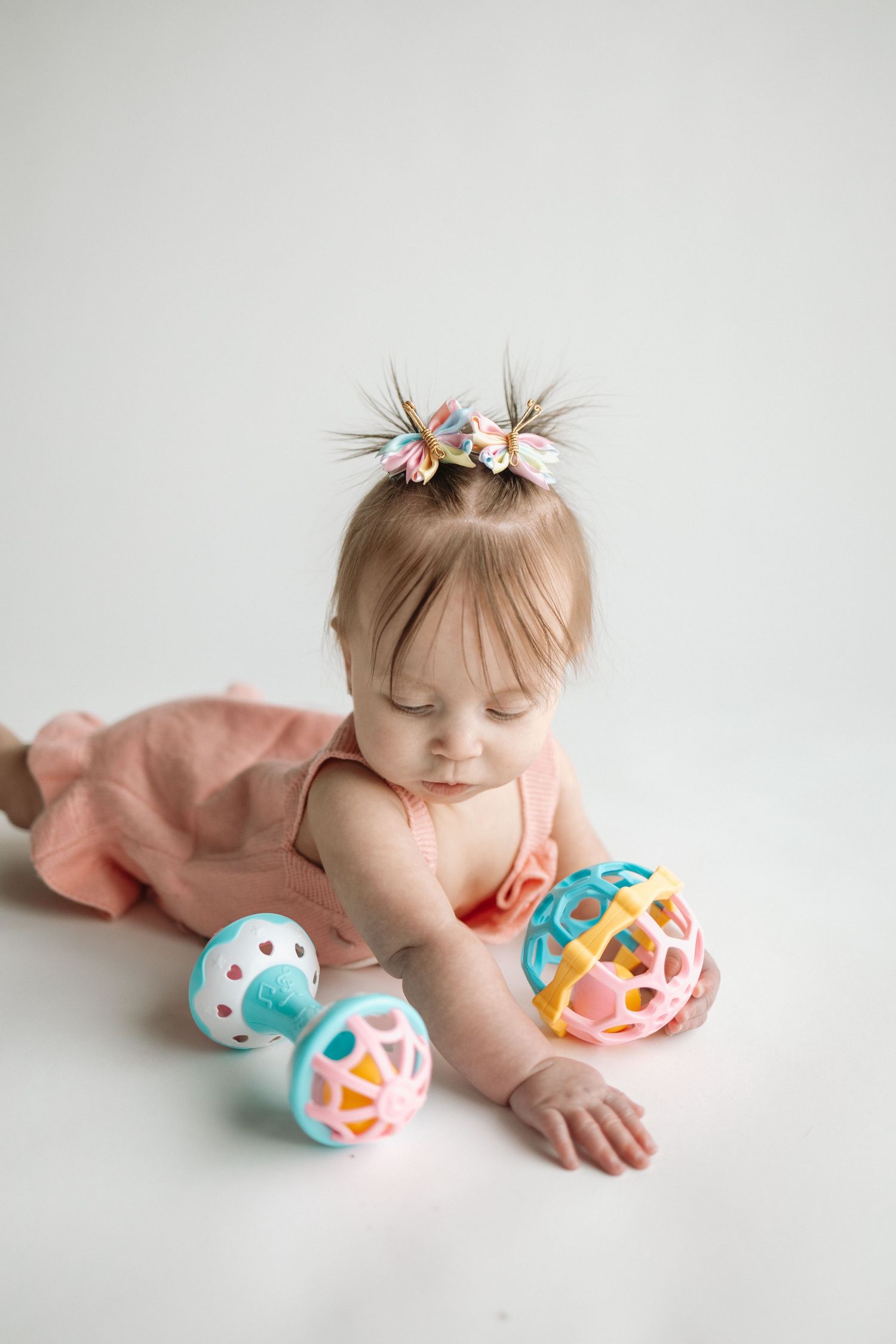 A baby in pink lying on a white background with colorful Easter eggs decorated in geometric patterns.