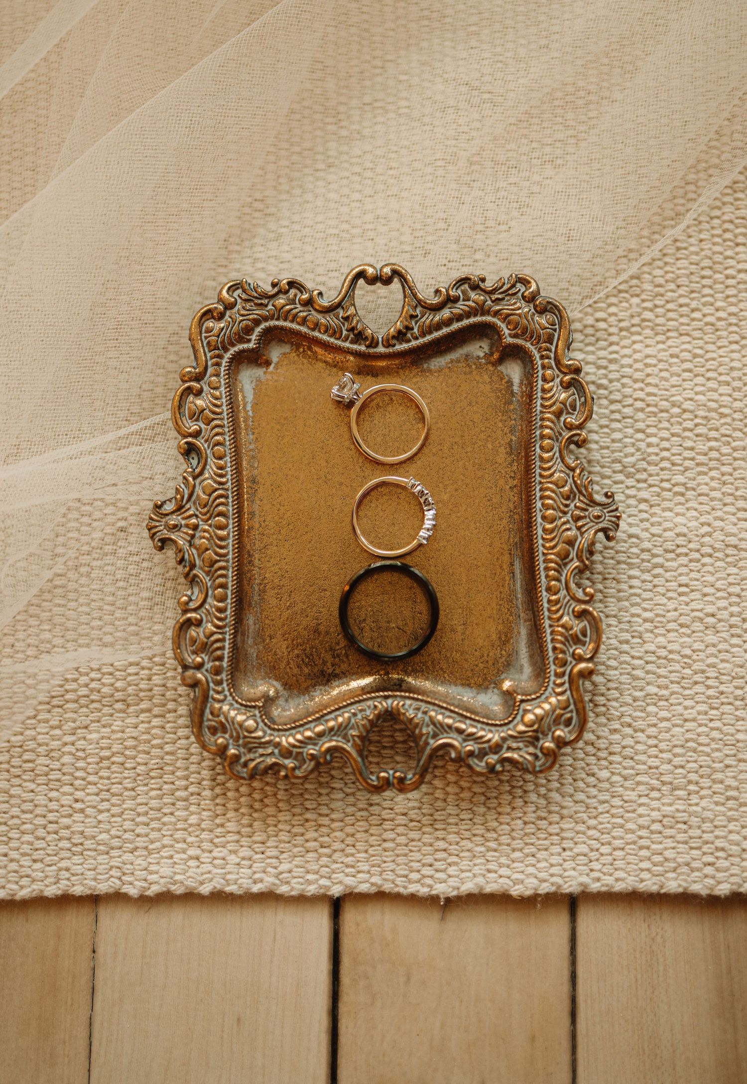 Five wedding rings displayed on an ornate gold vintage frame against a cream colored fabric backdrop.