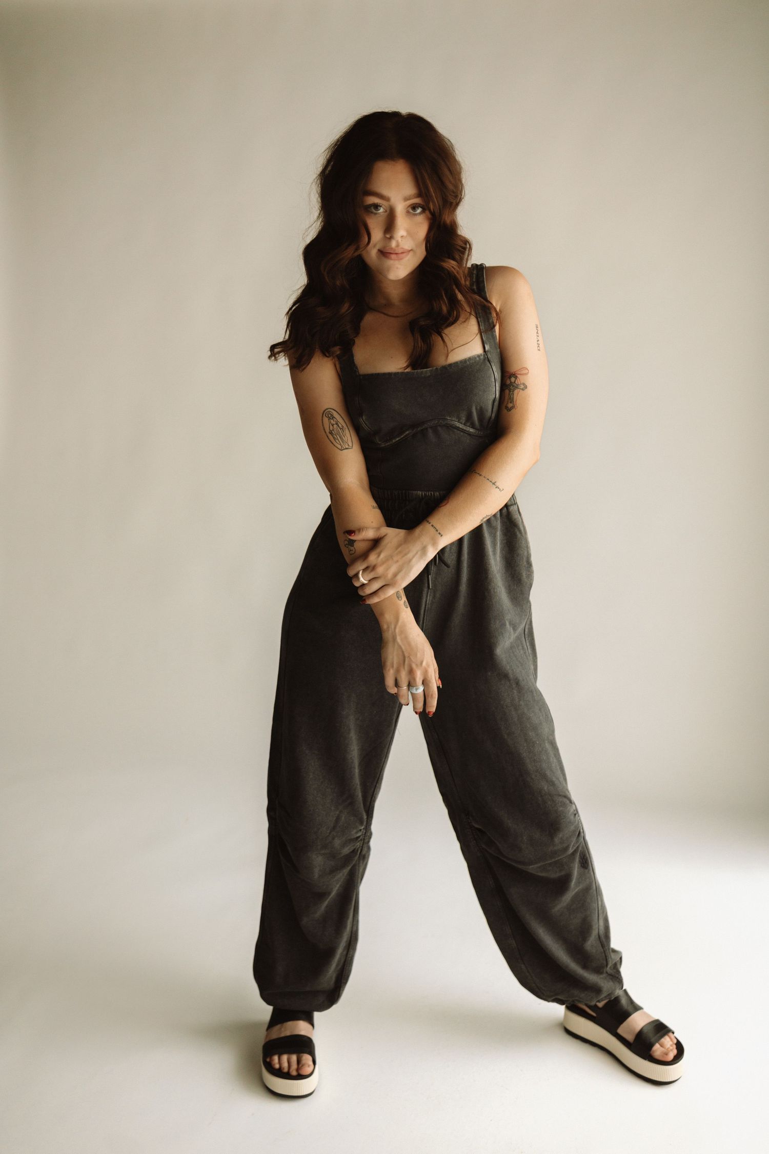 Five photos show a person wearing a loose black linen jumpsuit and sandals while posing casually against a white background.