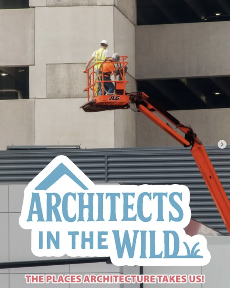 Two construction workers in bright safety vests operate a cherry picker lift while installing signage on a building exterior.