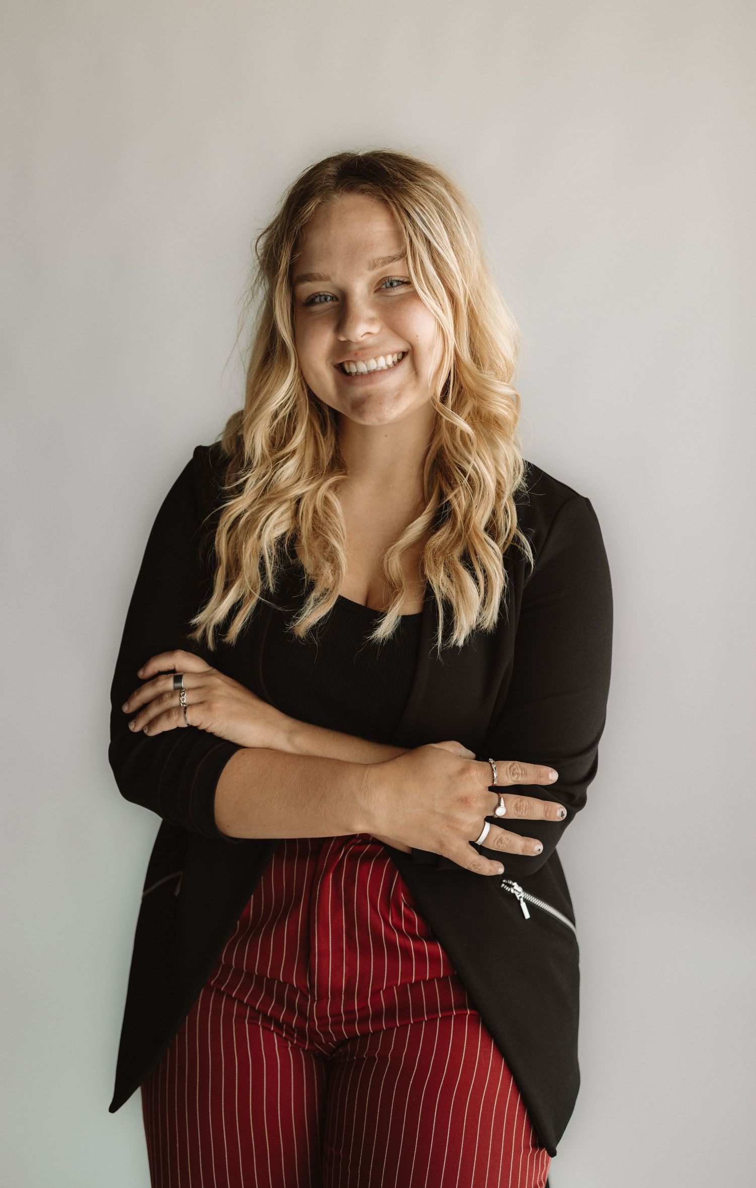 Professional portrait of a woman in a black blazer and red striped pants against a light gray background.