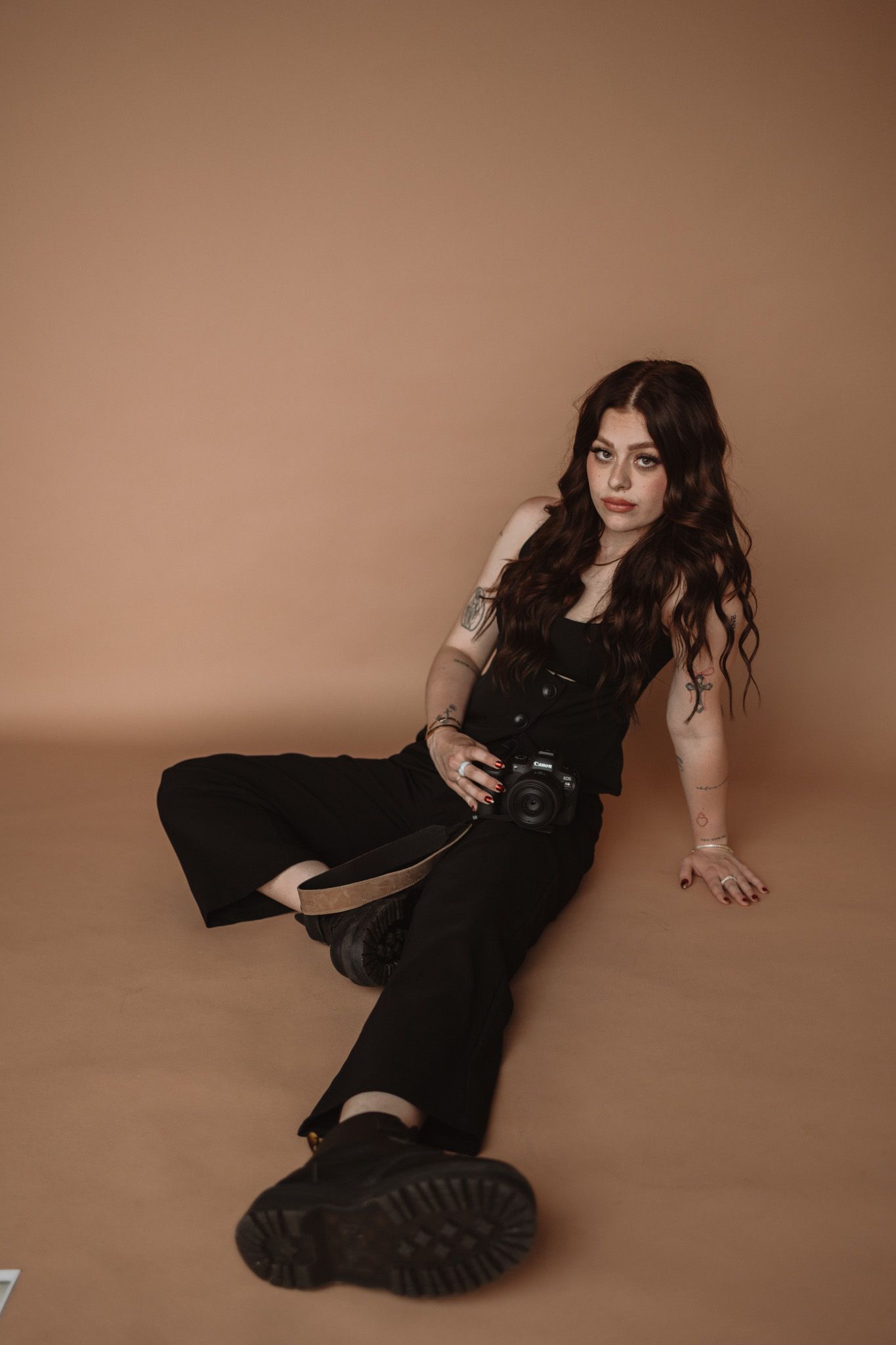 A figure in black clothing poses dramatically against a brown background in a moody portrait series.