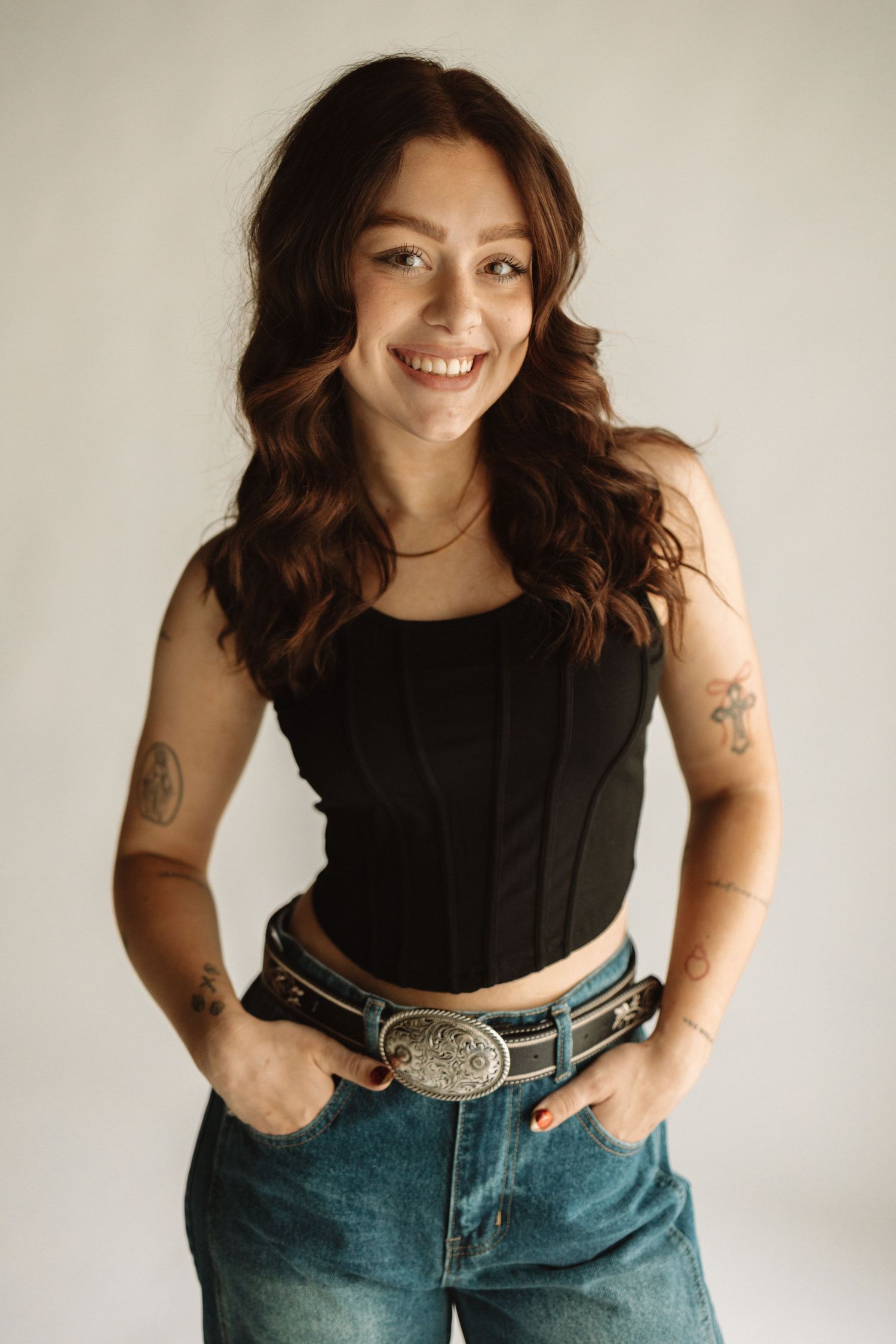 Woman in black sleeveless top and blue jeans poses against white backdrop in fashion photoshoot series.