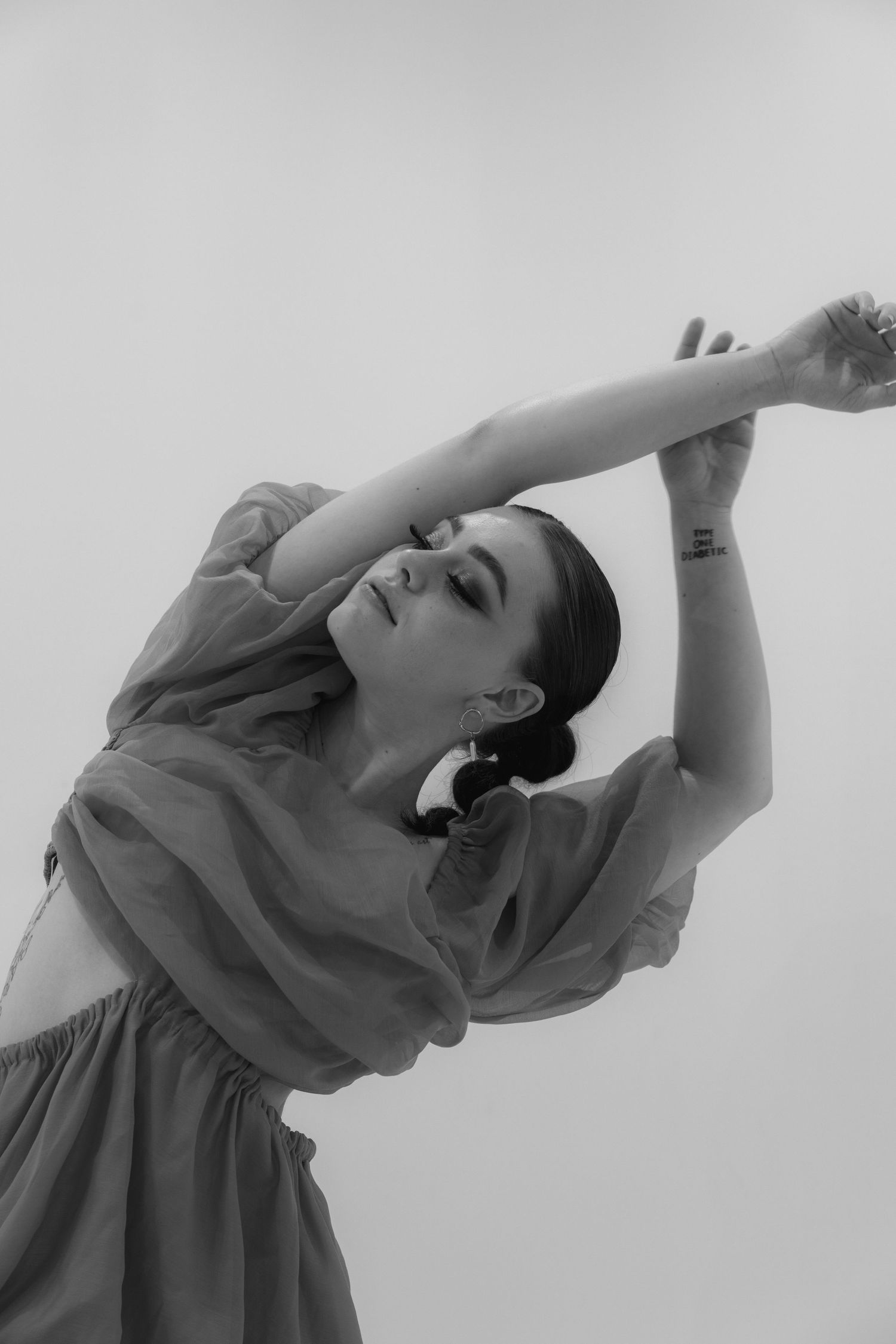 A graceful black and white portrait of a dancer in a flowing dress stretching upward with dramatic movement.