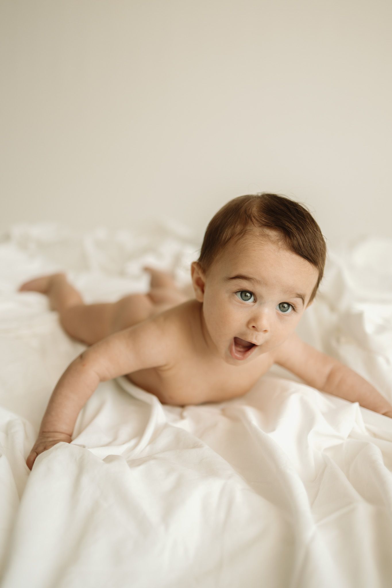 Sweet baby lying on white sheets with a playful expression during a lifestyle photo session.