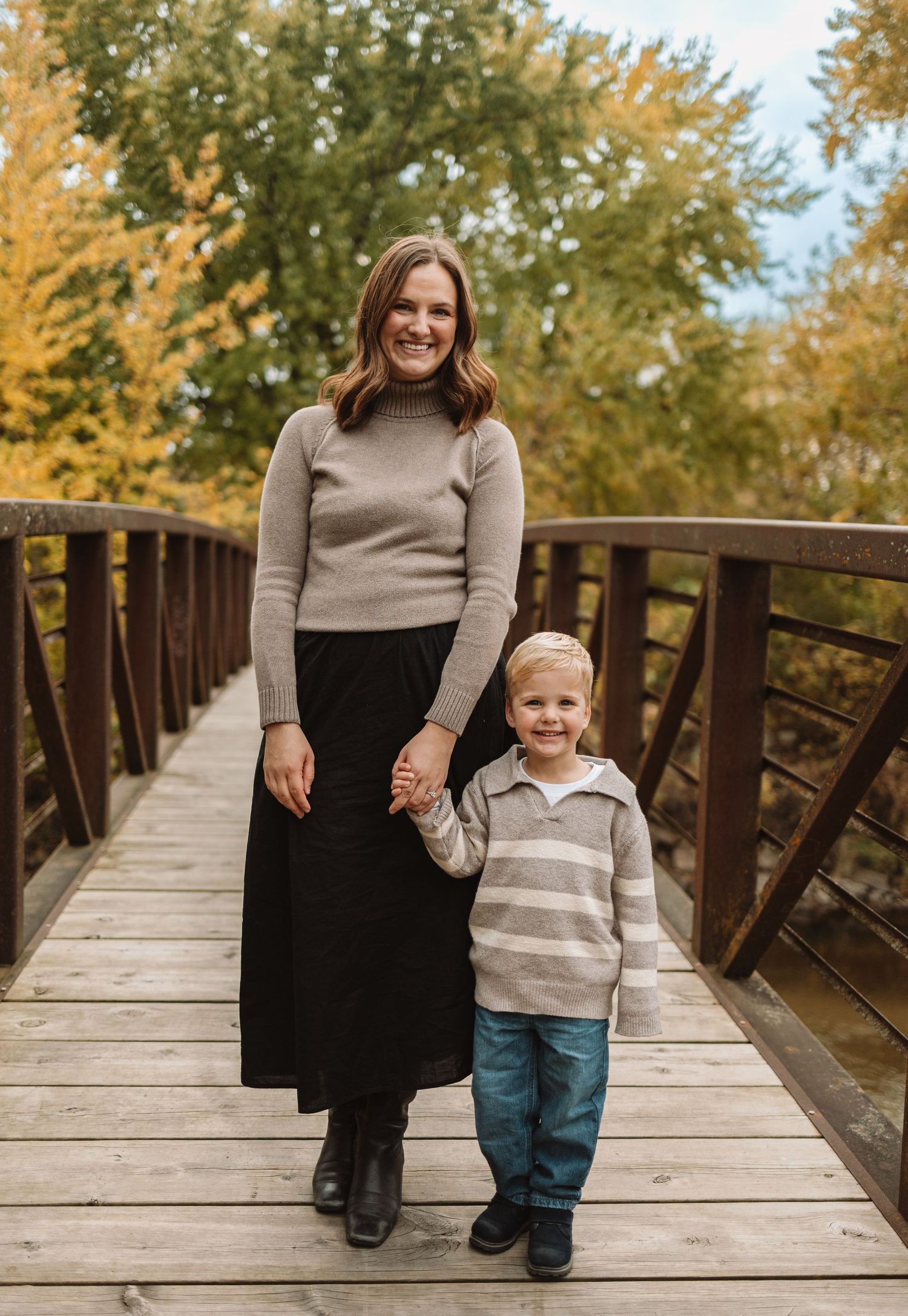A series of autumn family portraits taken on a wooden bridge with golden fall foliage in the background.