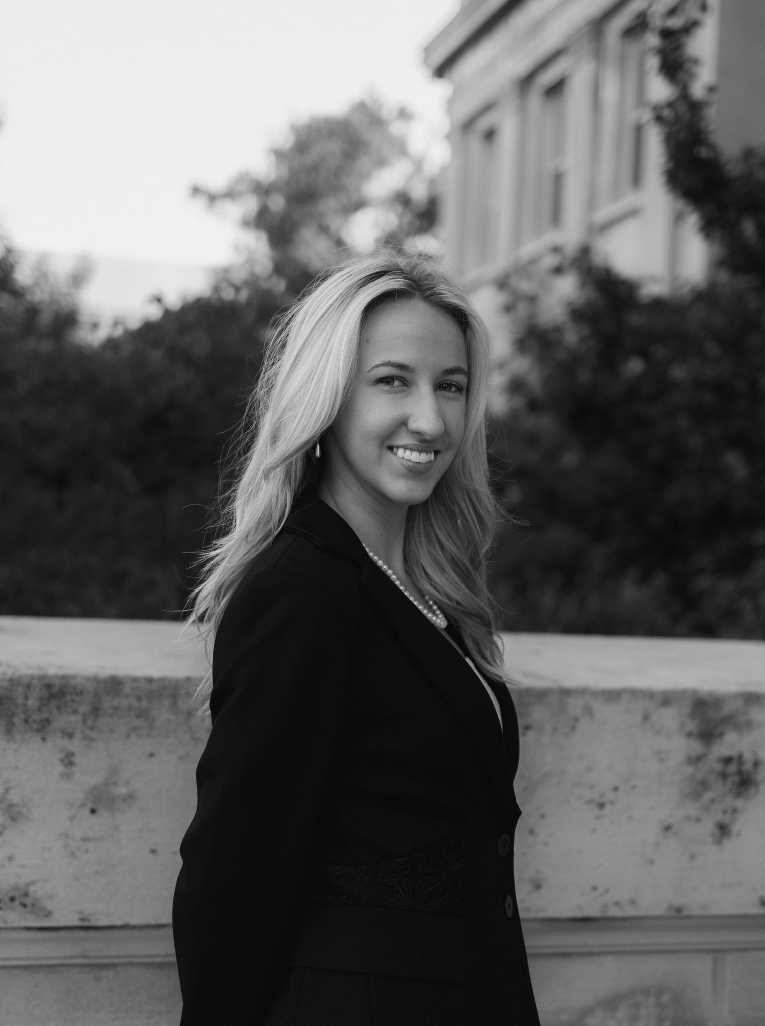 Black and white portrait series shows a woman in dark clothing smiling against an urban backdrop in natural lighting.