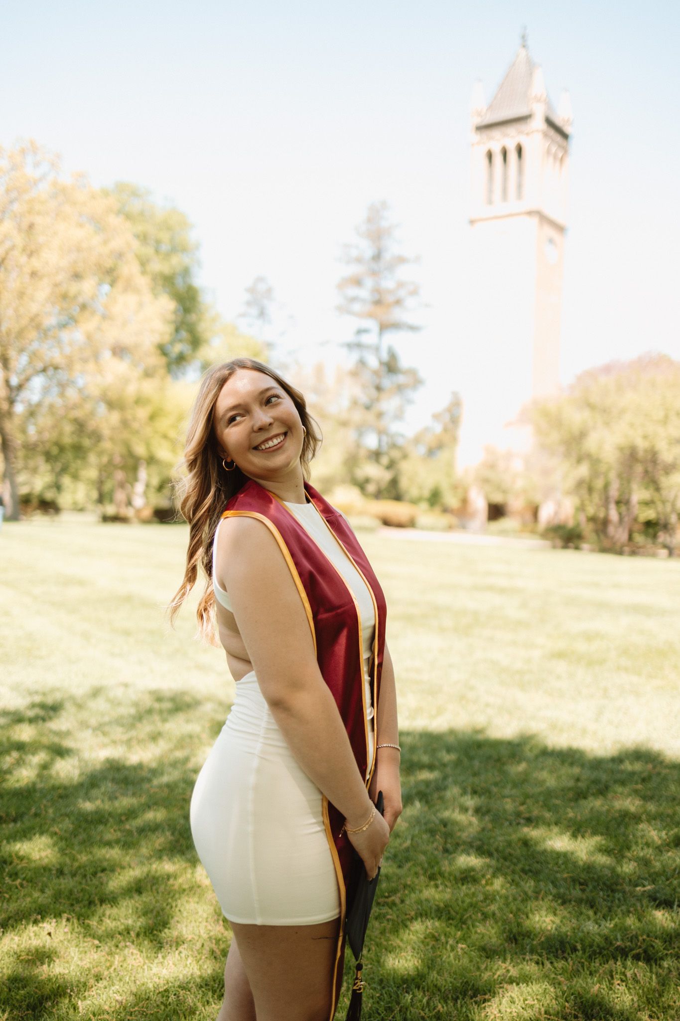 Expectant woman poses outdoors on grassy lawn with a church steeple visible in the background.