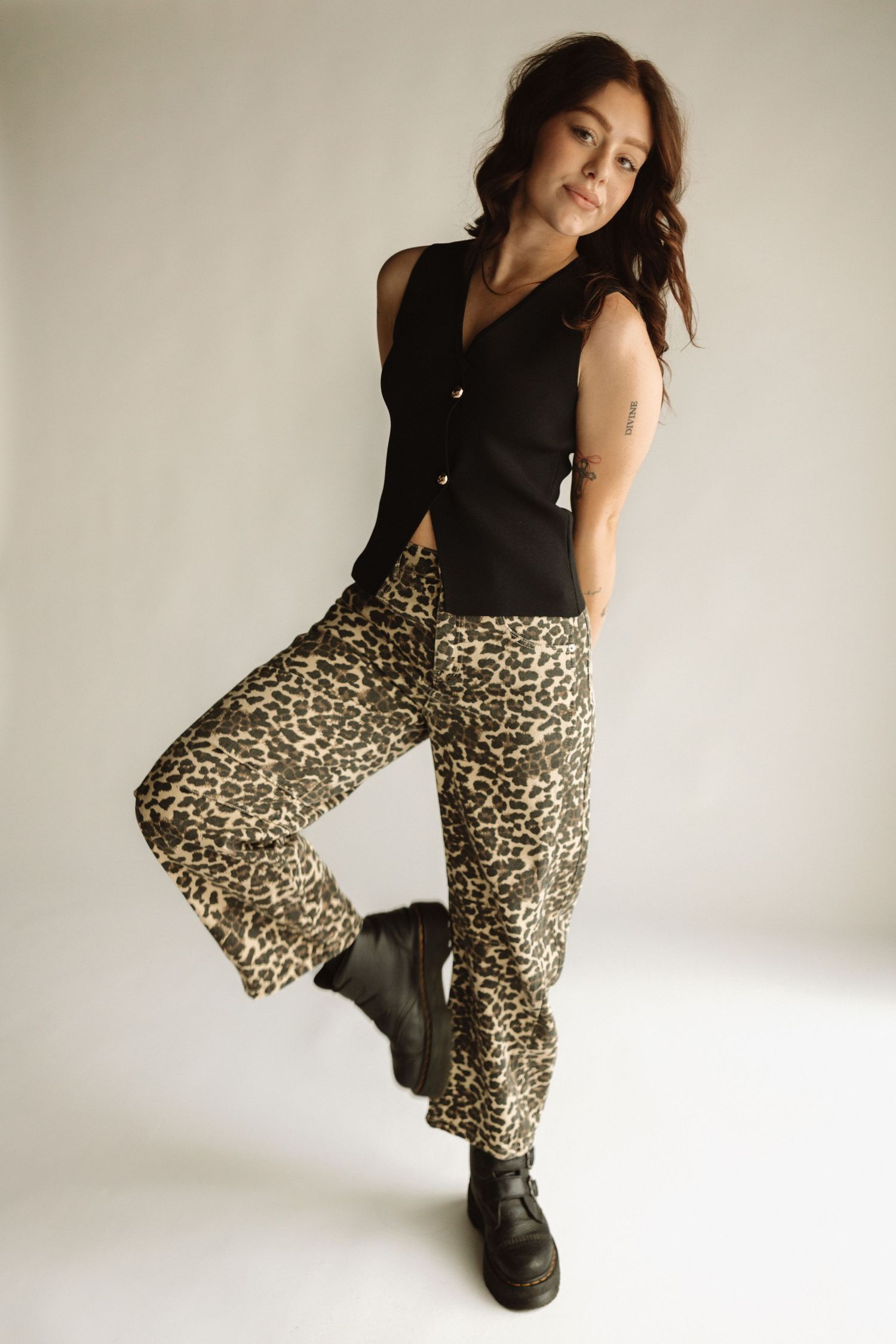 Fashion model wearing black sleeveless top and leopard print wide-leg pants with chunky black boots against white background.