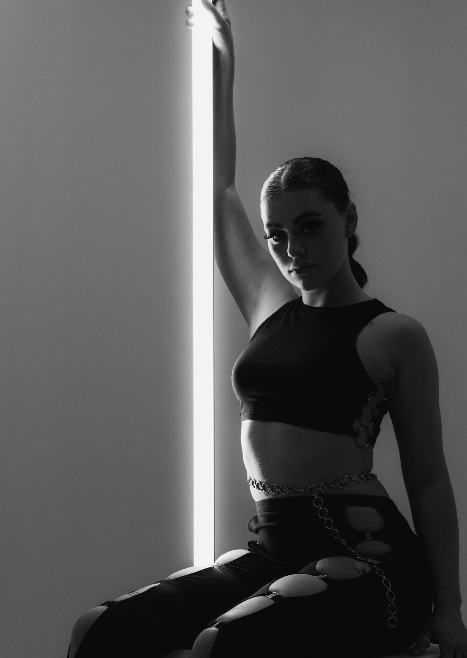 Dramatic black and white portrait with strong contrast lighting featuring a figure in athletic wear against a bright vertical light source.
