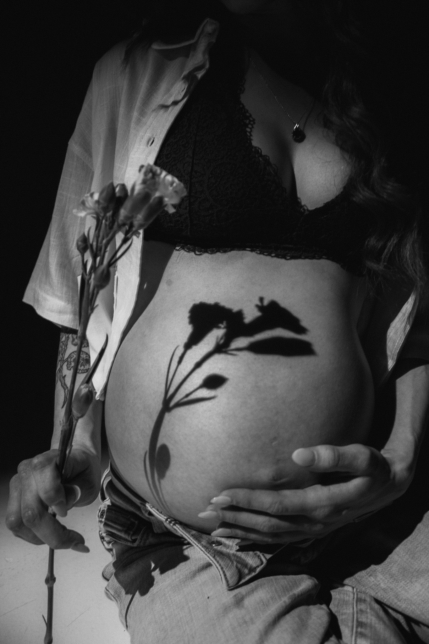 Maternity photo series with flowers against pregnant belly in dark lighting.