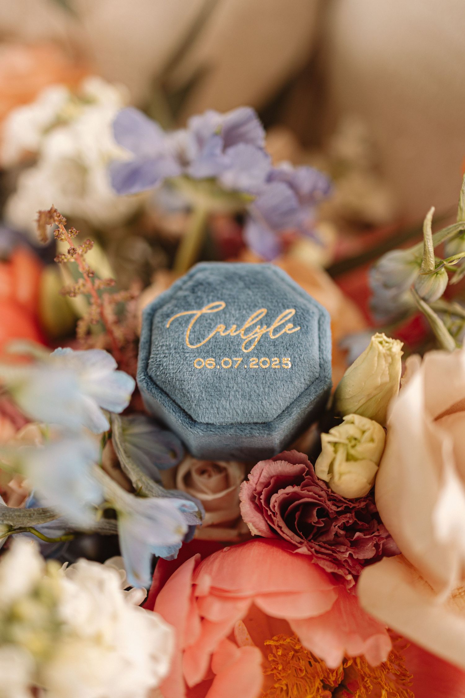Close-up of wedding rings on denim blue tags nestled among pink, burgundy and white dried flowers.