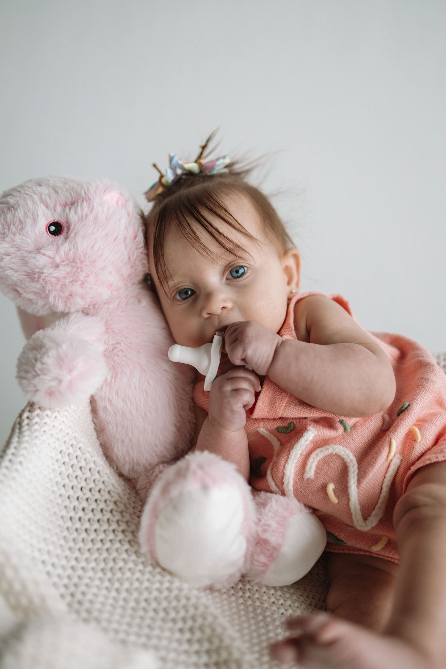 A soft pink plush bunny toy rests on white knitted fabric in a gentle nursery setting.