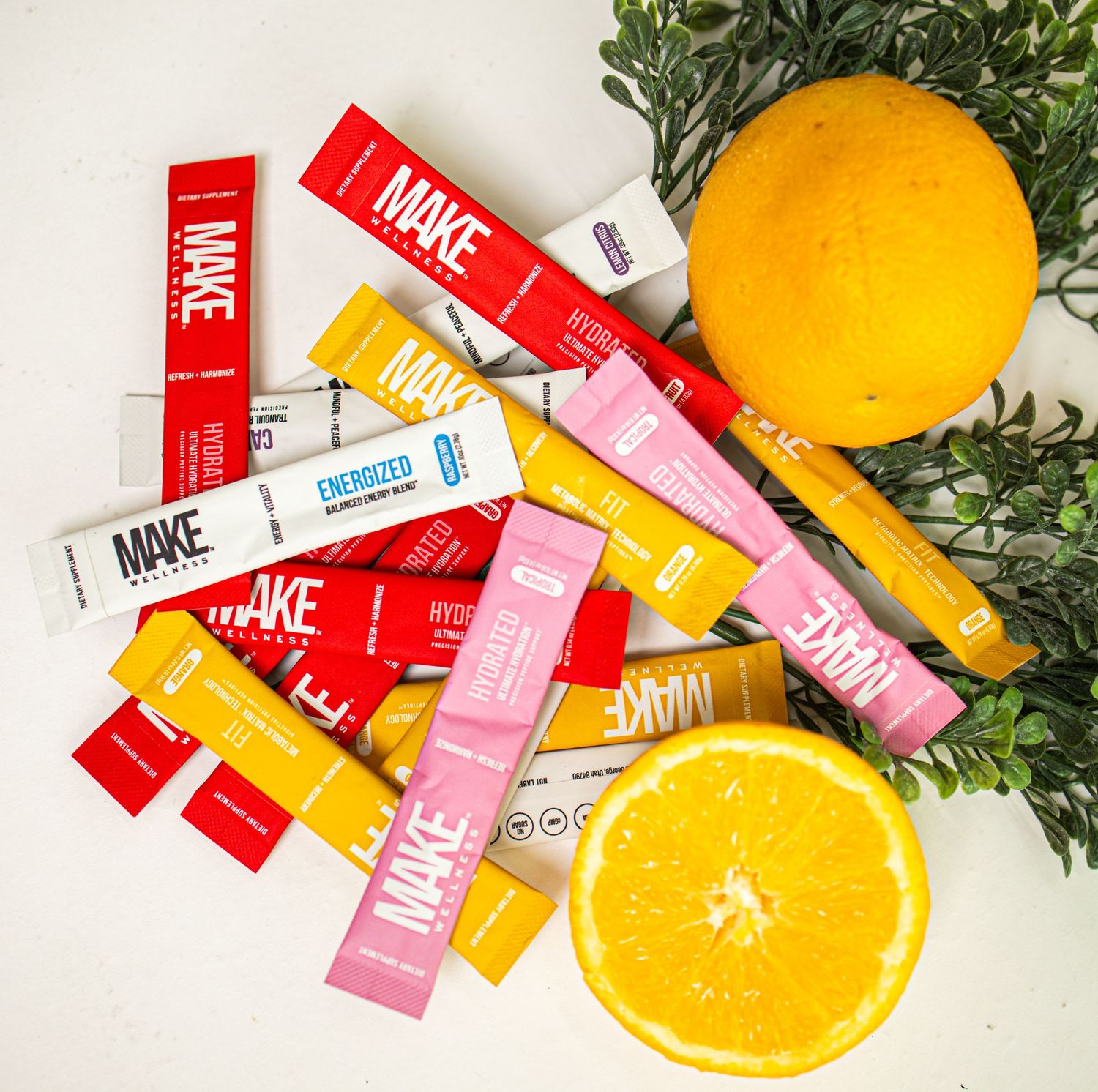 Colorful makeup products arranged with fresh citrus fruits and green herbs on white surface.