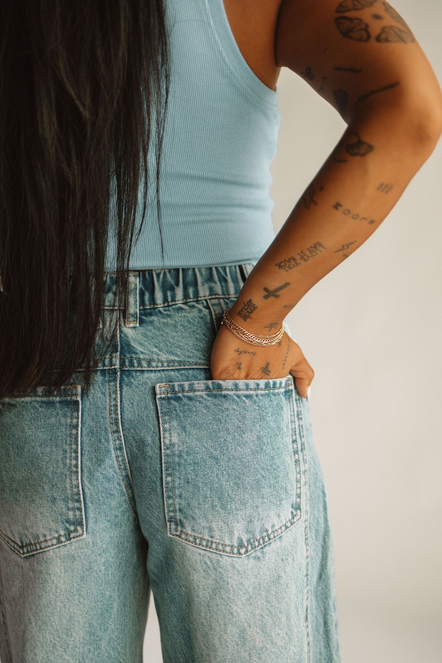 Side view of light blue tank top and loose-fit jeans outfit with visible arm tattoos and silver bracelet.