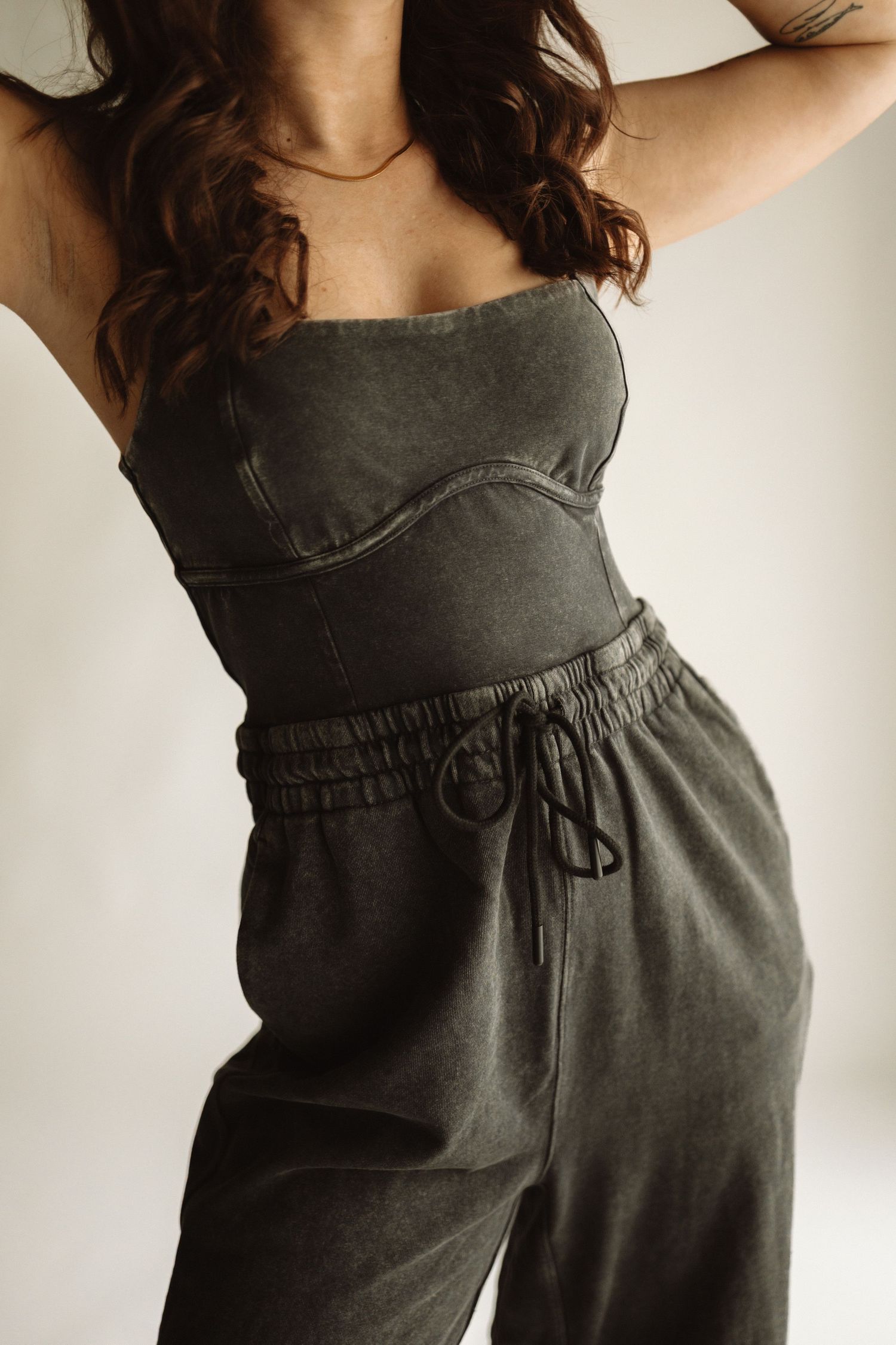 Woman wearing an olive green corset top and matching drawstring pants in a minimalist indoor setting.