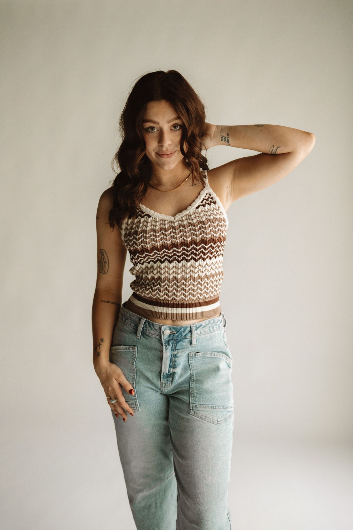 Model posing in a brown and cream crochet crop top with light wash jeans against a neutral background.