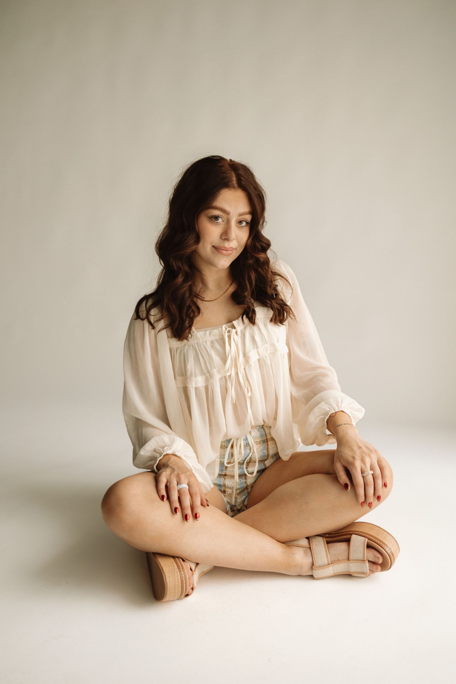 A person in a cream-colored vintage dress is elegantly posed against a light neutral background in an artistic series.