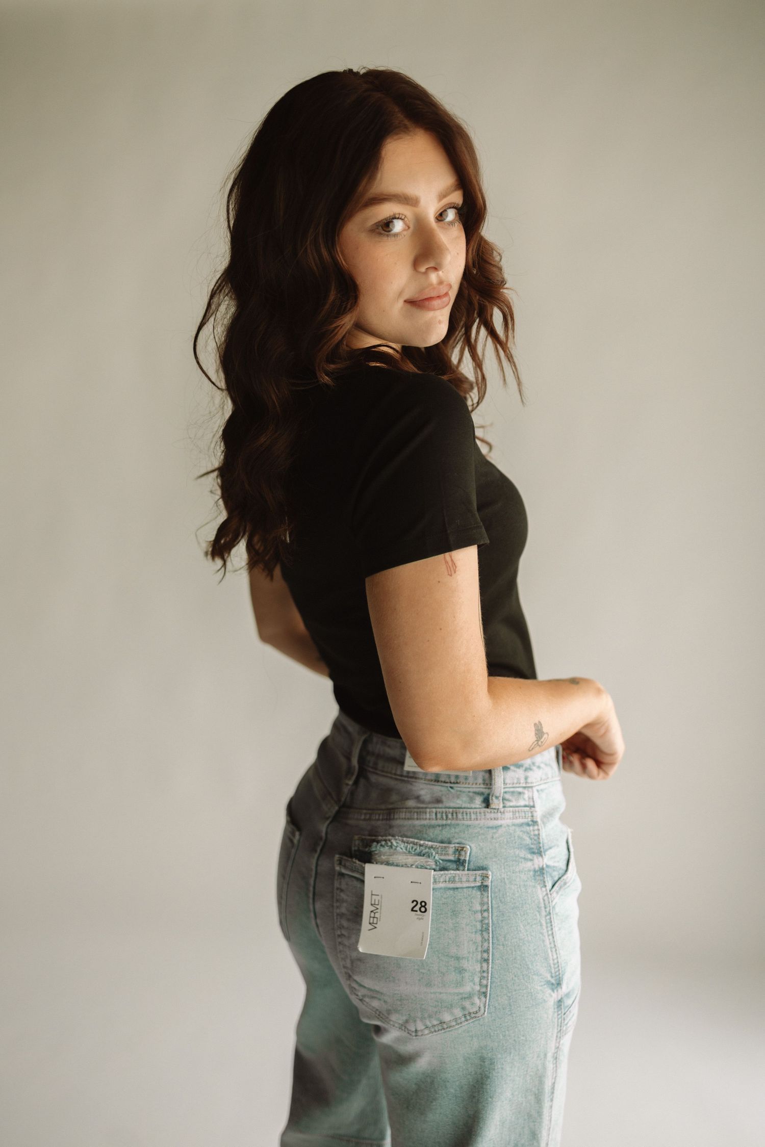 Woman wearing a black t-shirt and light wash jeans poses against white backdrop in multiple minimalist fashion shots.