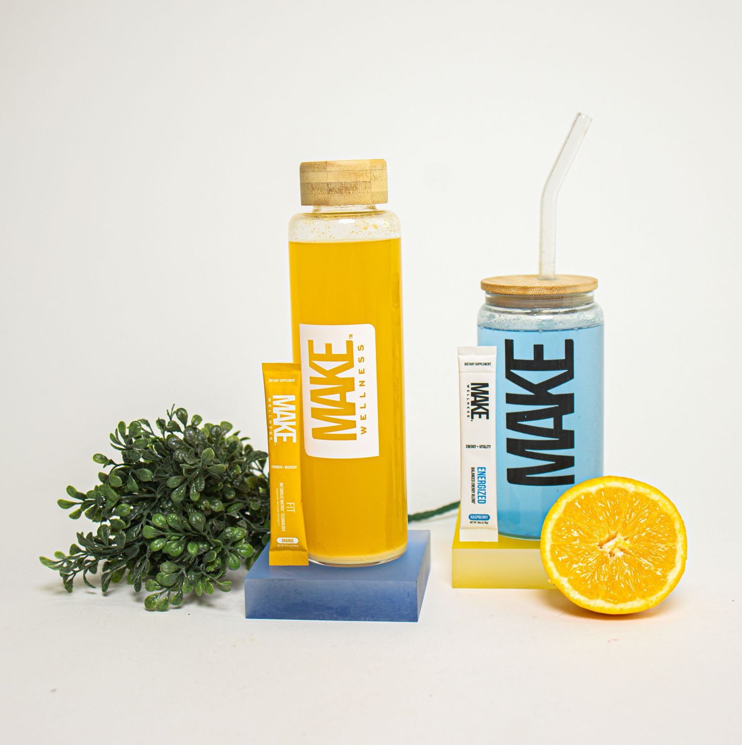 Minimalist product photography of glass bottles with orange juice and fresh herbs against white background.