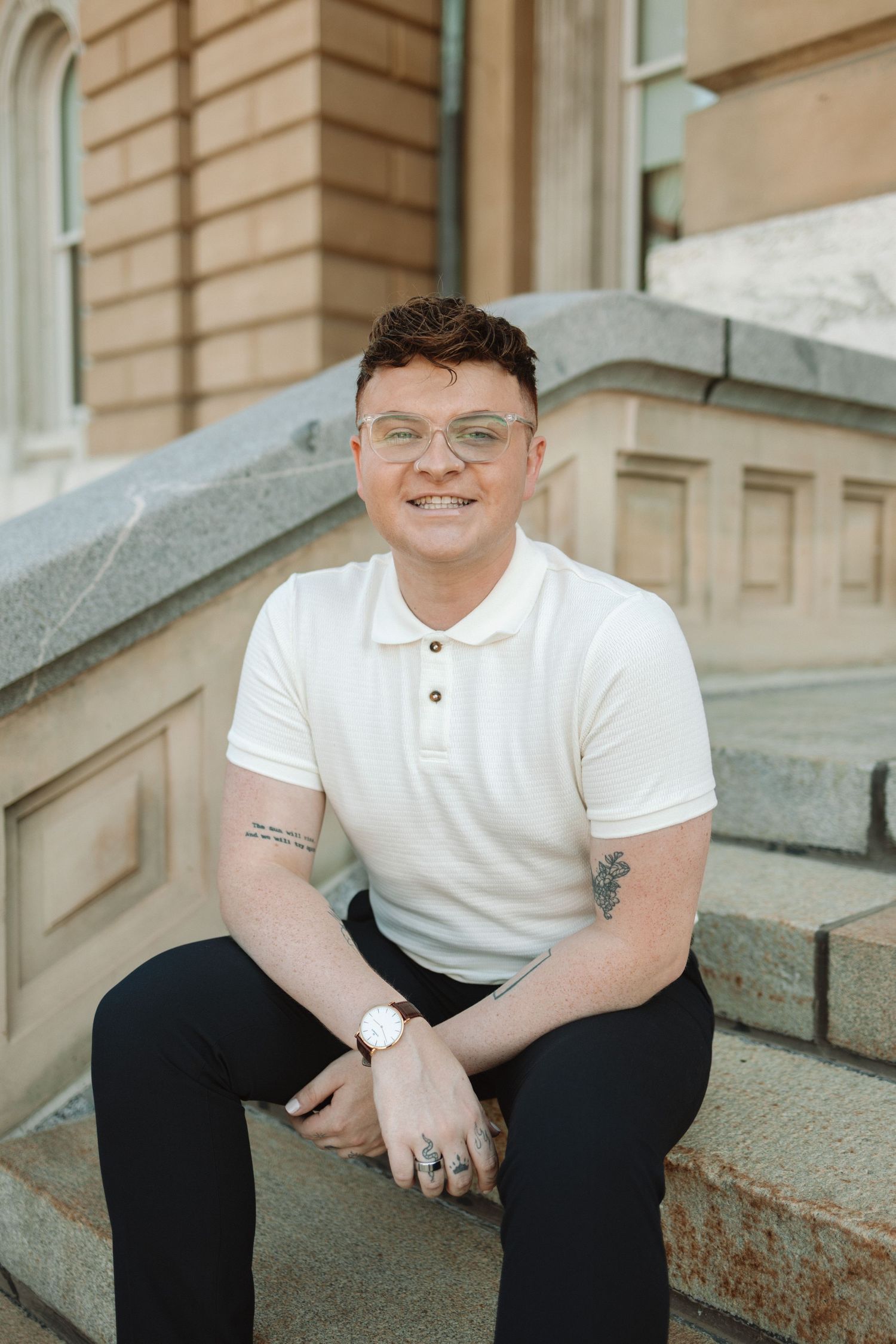 Person in white polo shirt sitting on stone steps with architectural details in background.