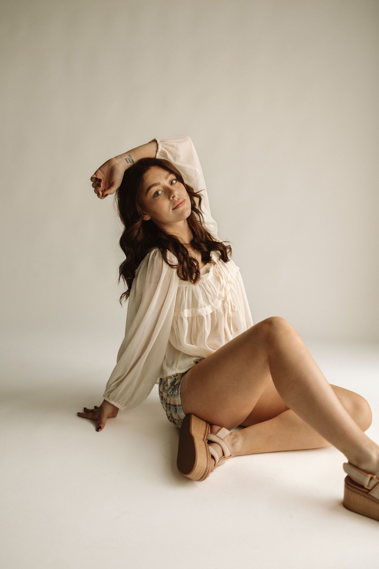 A person poses elegantly in a flowy white blouse while lying down in a minimalist setting with soft lighting.