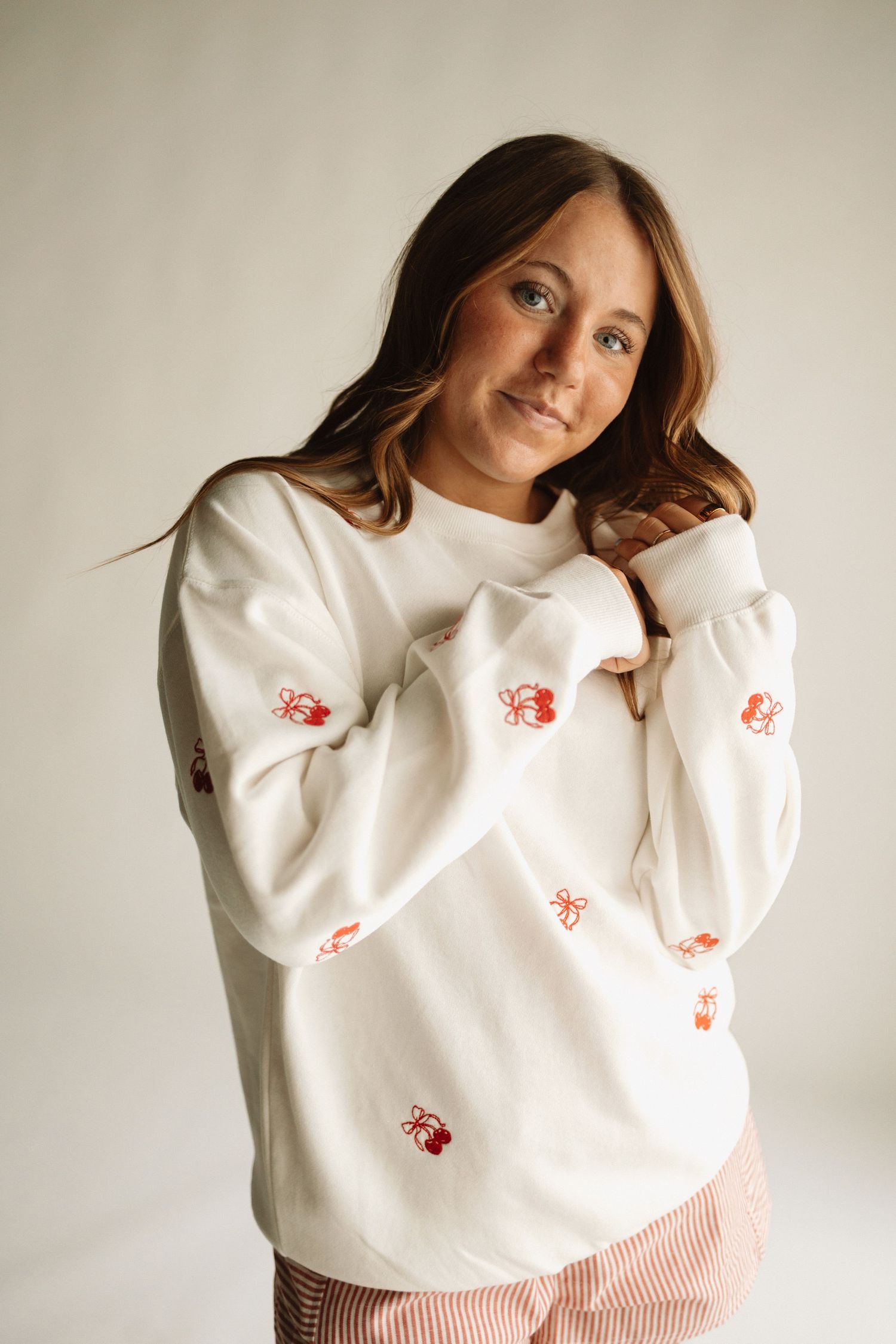 A white pullover sweater with red floral embroidery shown in multiple angles against a neutral background.