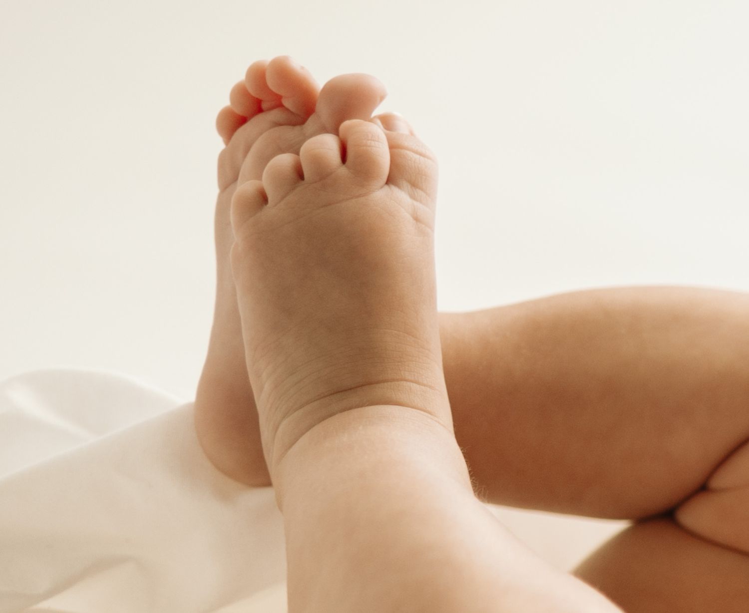 Close-up photo of a baby's tiny foot with chubby toes resting on soft white fabric.