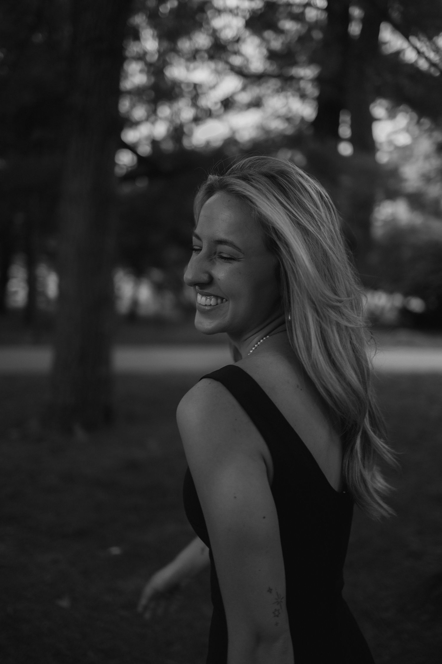 Black and white portrait series of a person laughing joyfully in a park setting with trees in the background.